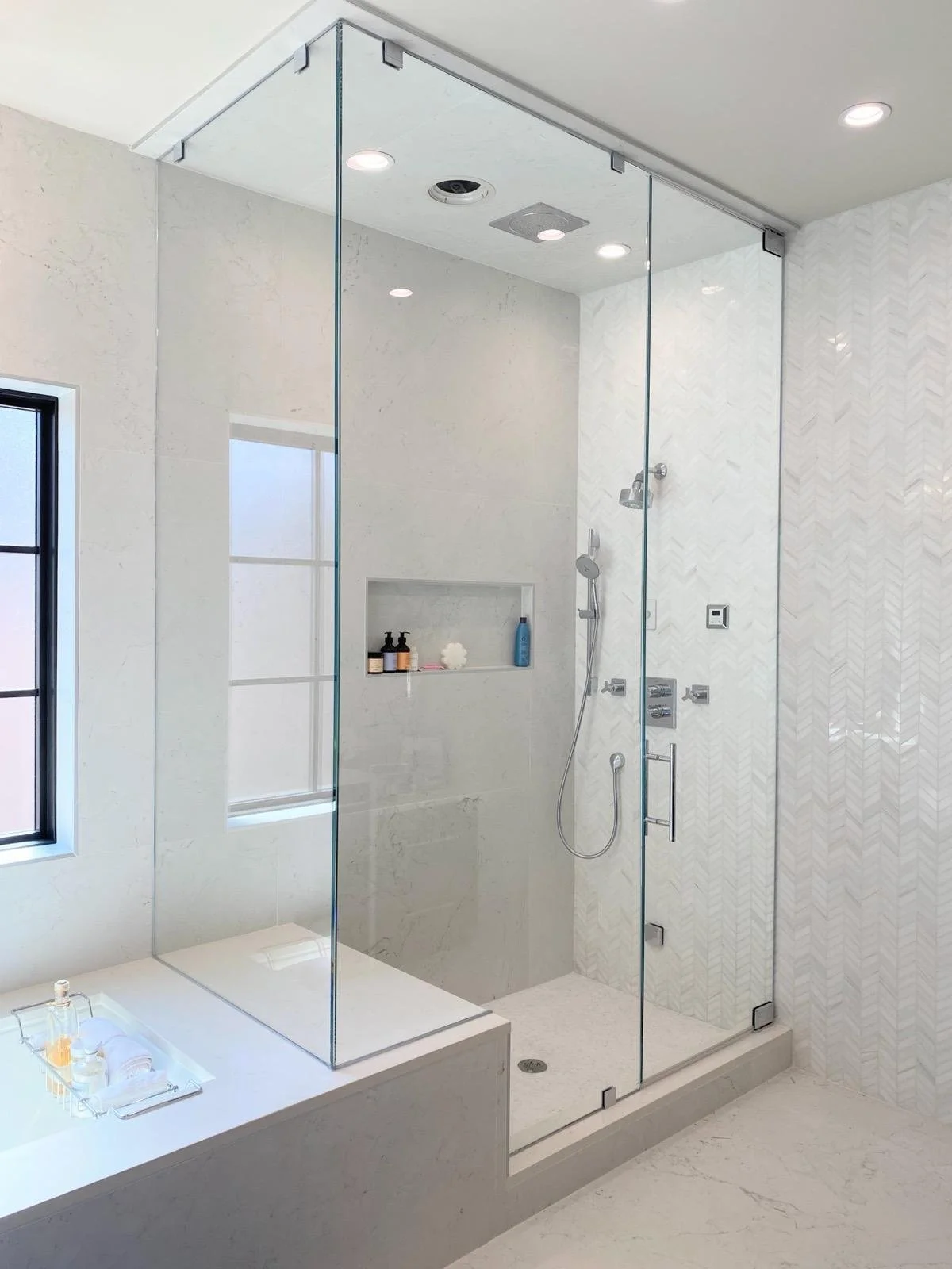 Modern walk-in glass shower with built-in niche and white marble walls in a bright bathroom.