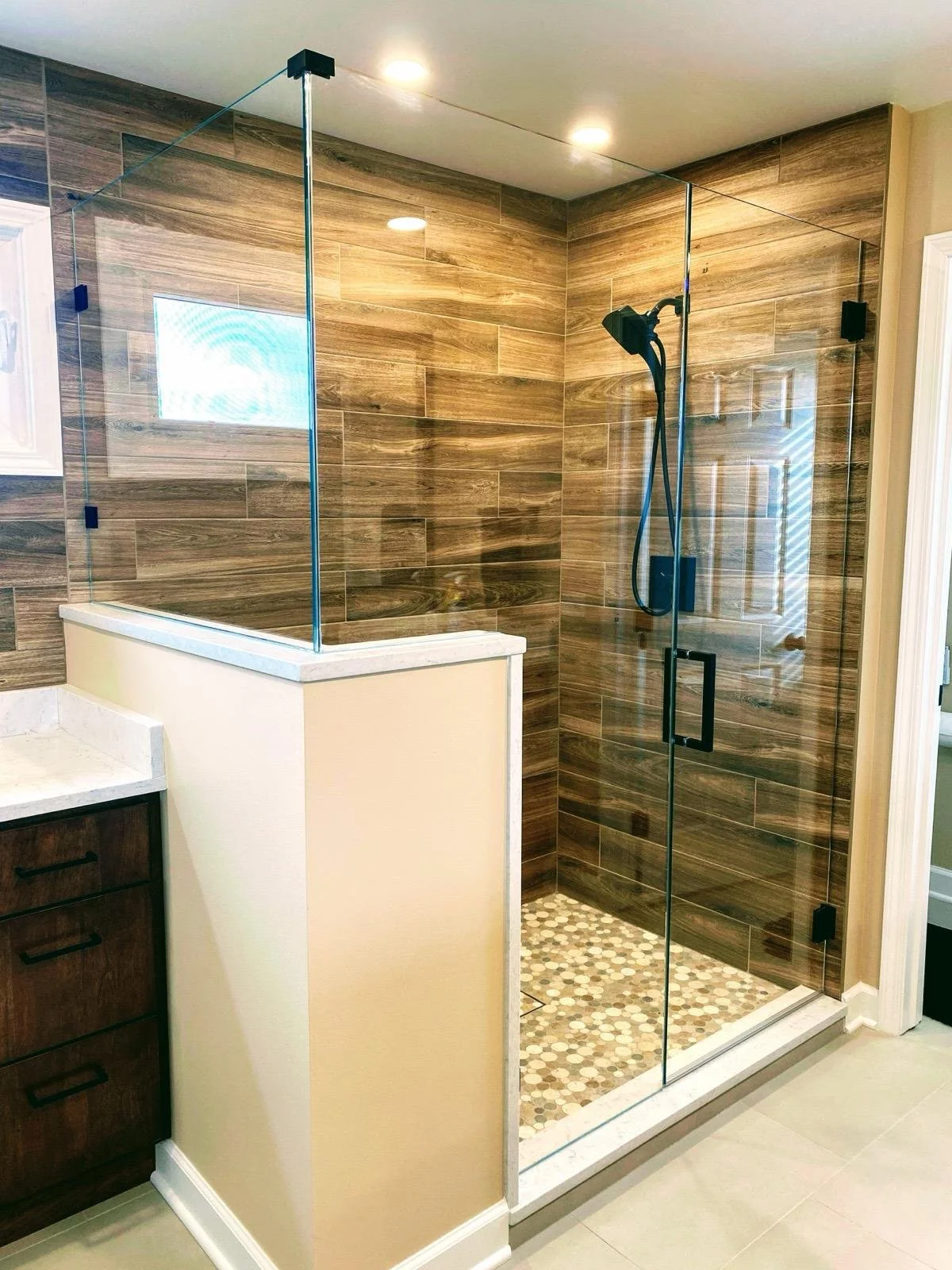 Bathroom with glass shower enclosure, wood-like wall tiles, and a pebble tile shower floor.