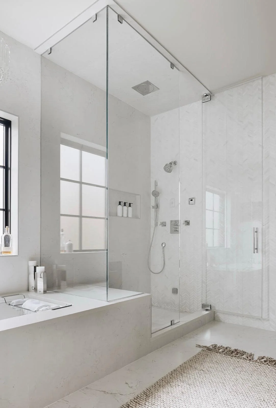 Modern white bathroom with a glass-enclosed shower, a bathtub, and a woven rug on the floor.