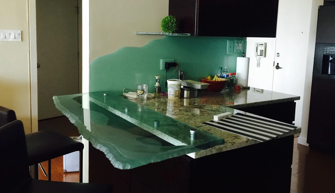 Kitchen with a green countertop and a natural edge glass bar top, various bottles and kitchen items, a paper towel roll, and a bowl of fruit.