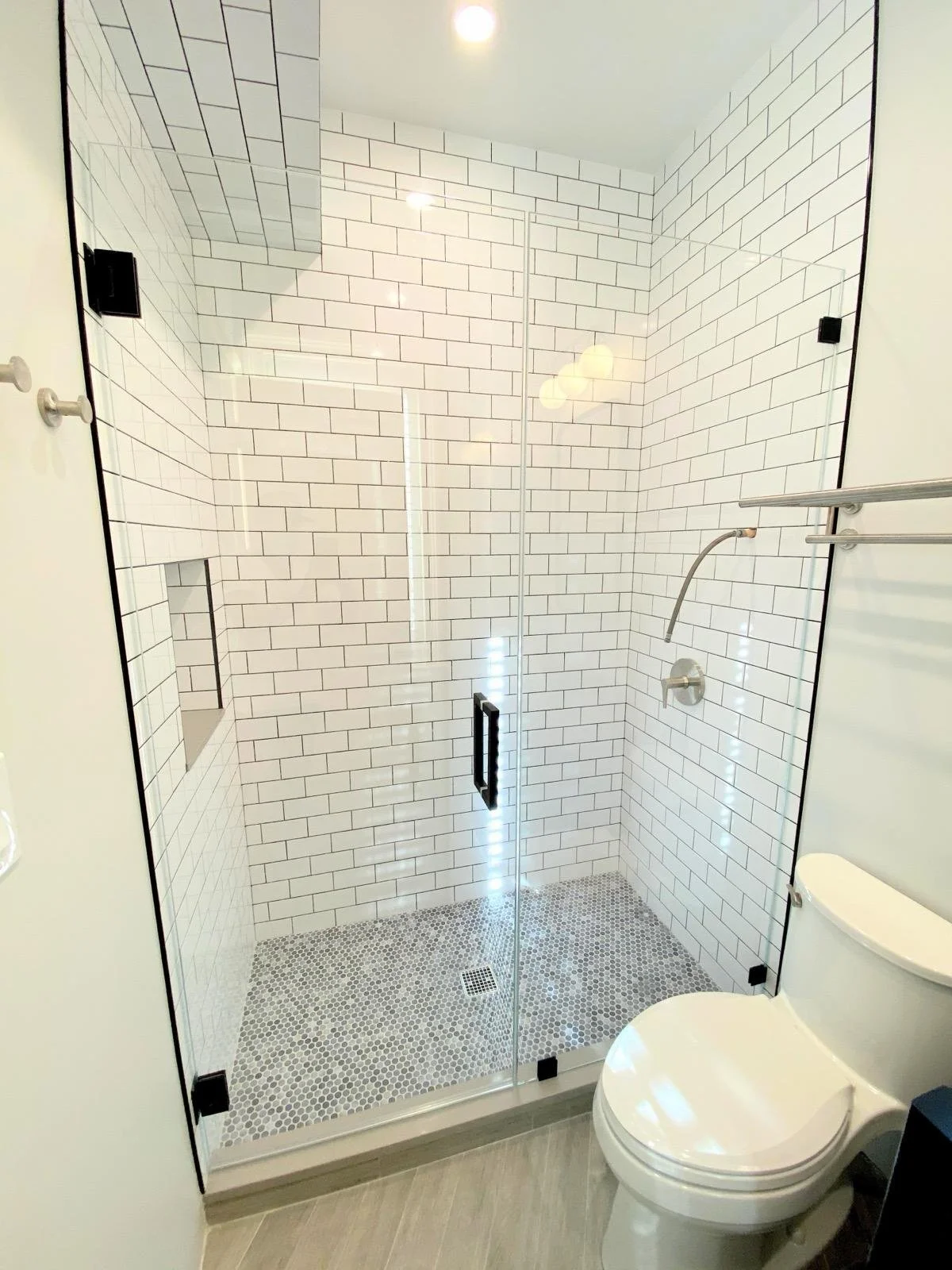 A modern bathroom with a glass shower enclosure with white subway tile walls and pebble tile floor, and a white toilet in the corner.