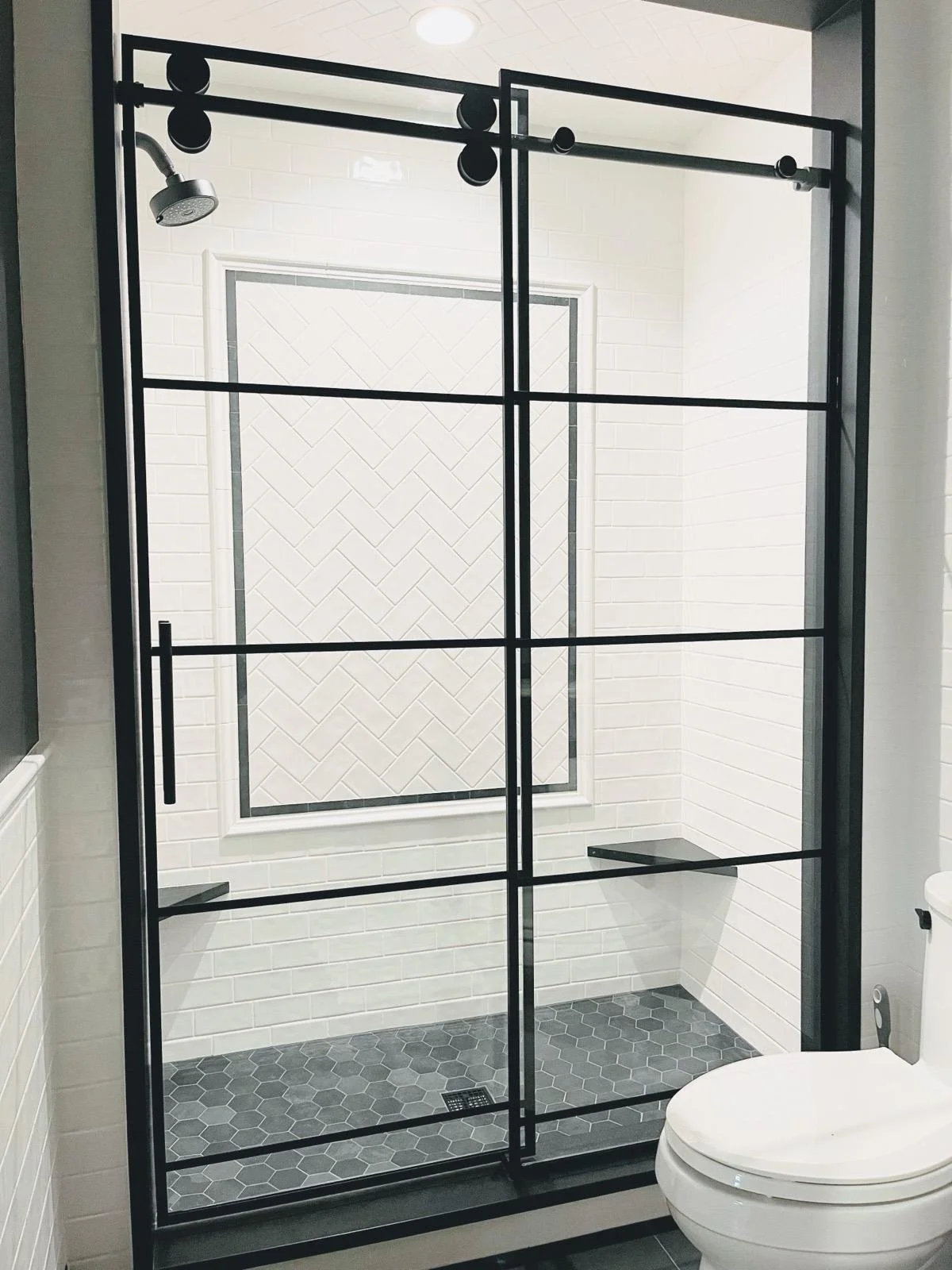 Modern bathroom with a black-framed glass shower door, white subway tiles, a herringbone tile accent, and a toilet in the foreground.