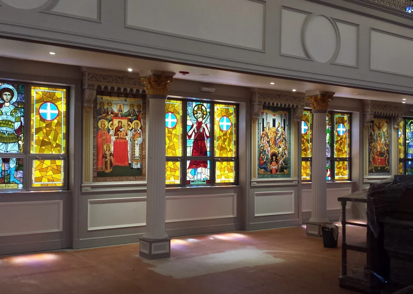 Interior of a church with colorful stained glass windows depicting religious scenes and figures, supported by white columns with gold accents.