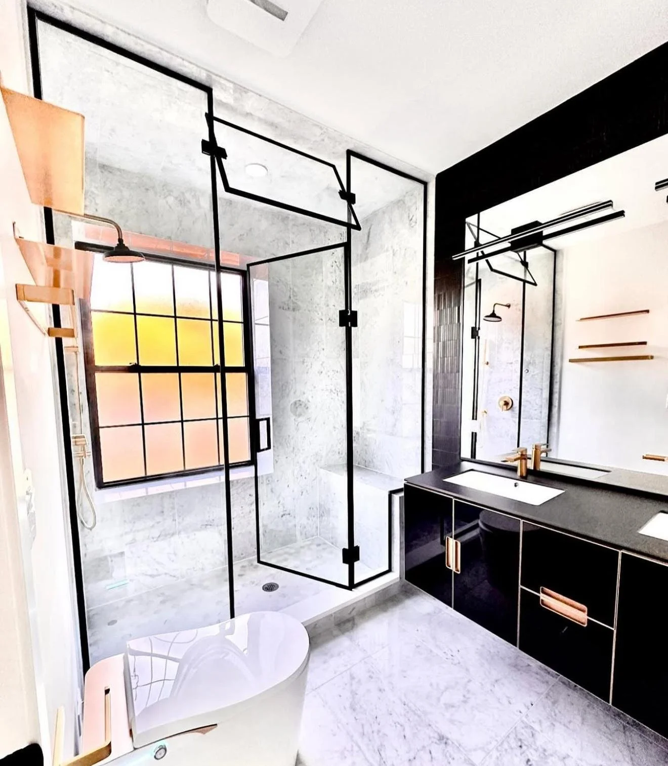 Modern bathroom with black-framed glass shower, double vanity with dark countertop and gold fixtures, freestanding bathtub, marble floors, and large window with black grid.