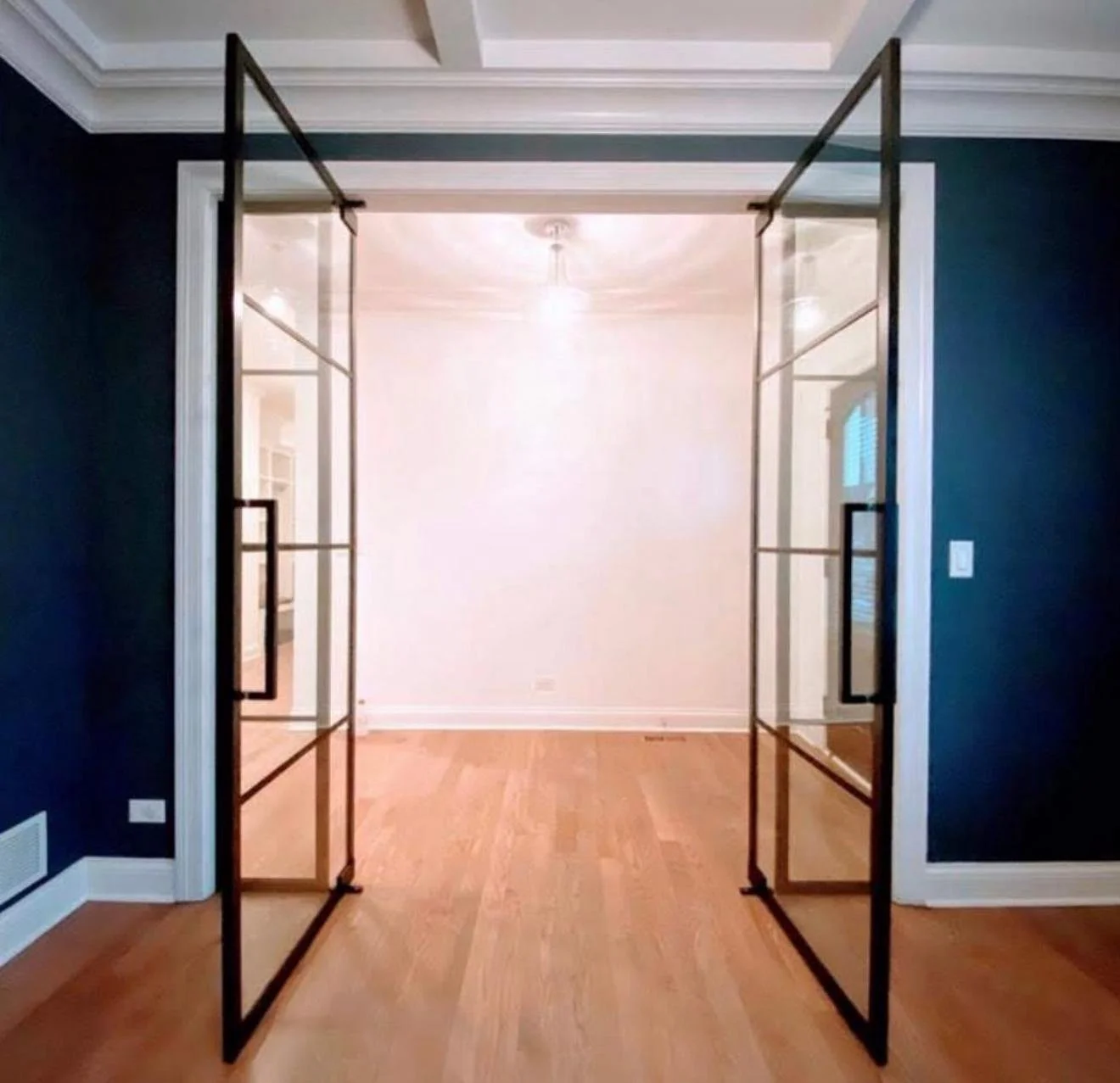 Open glass doors leading into a brightly lit room with light-colored walls and hardwood flooring.