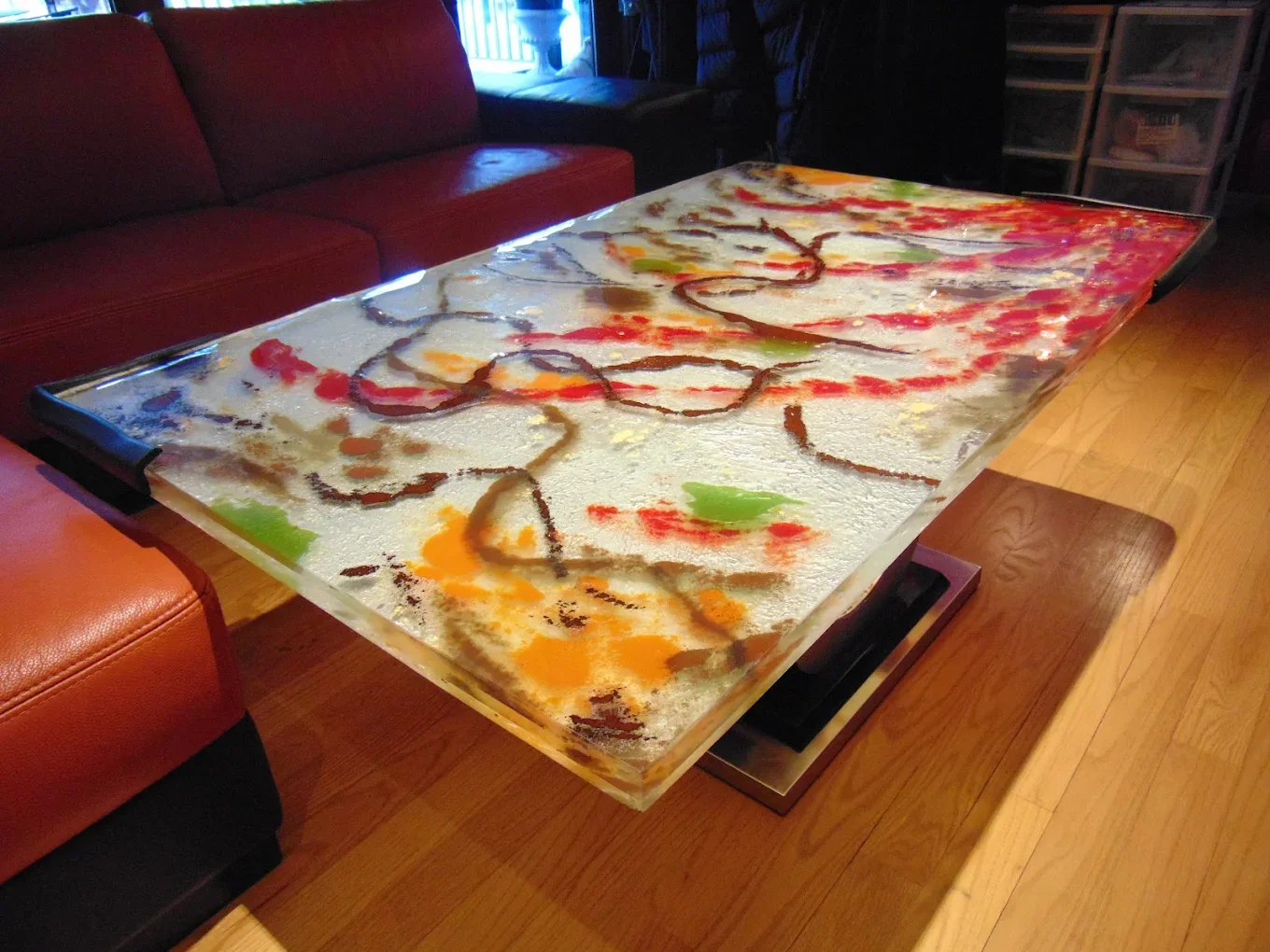 Decorative tabletop with colorful abstract design, featuring red, green, yellow, and orange accents, placed in a living room with a red couch and wooden floor.