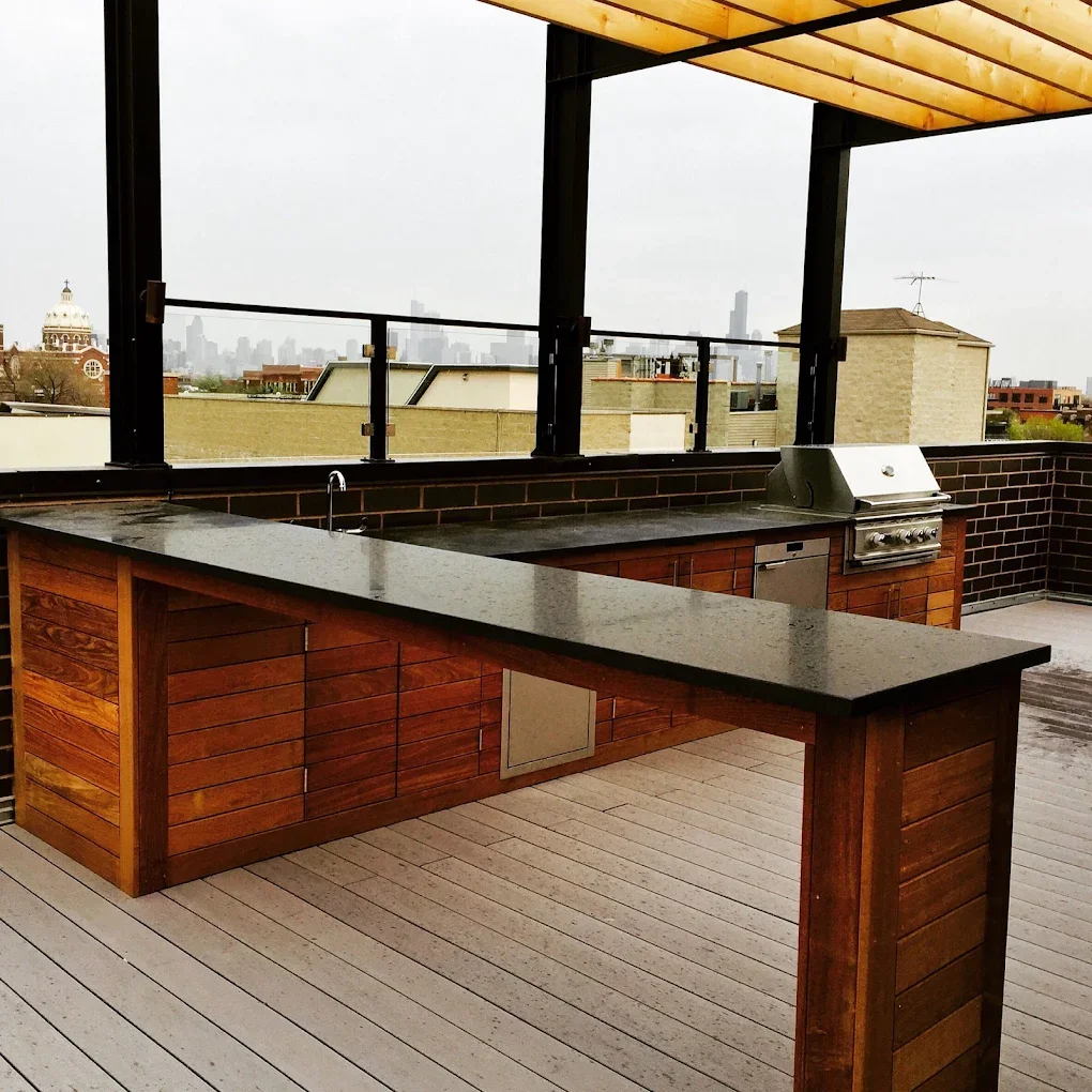 Outdoor rooftop kitchen with a wooden counter, built-in grill, and a view of the city skyline in the background.