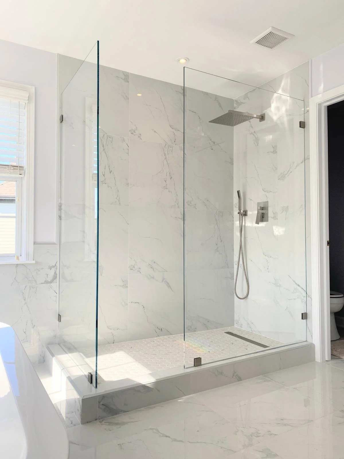 Modern bathroom with a glass-enclosed walk-in shower with marble walls and a rain shower head.