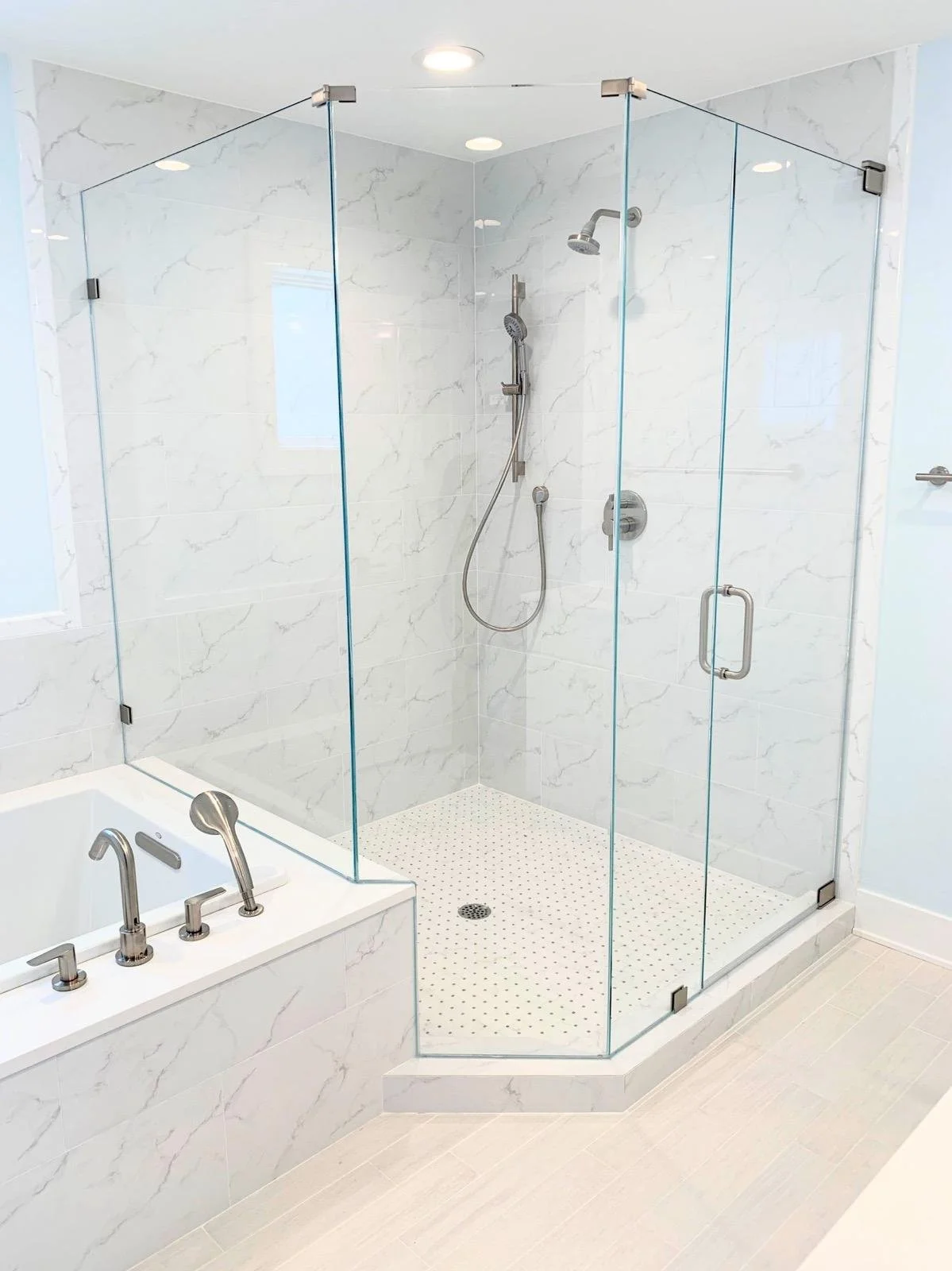 A modern bathroom with a glass-enclosed walk-in shower and a white marble bathtub with silver fixtures.