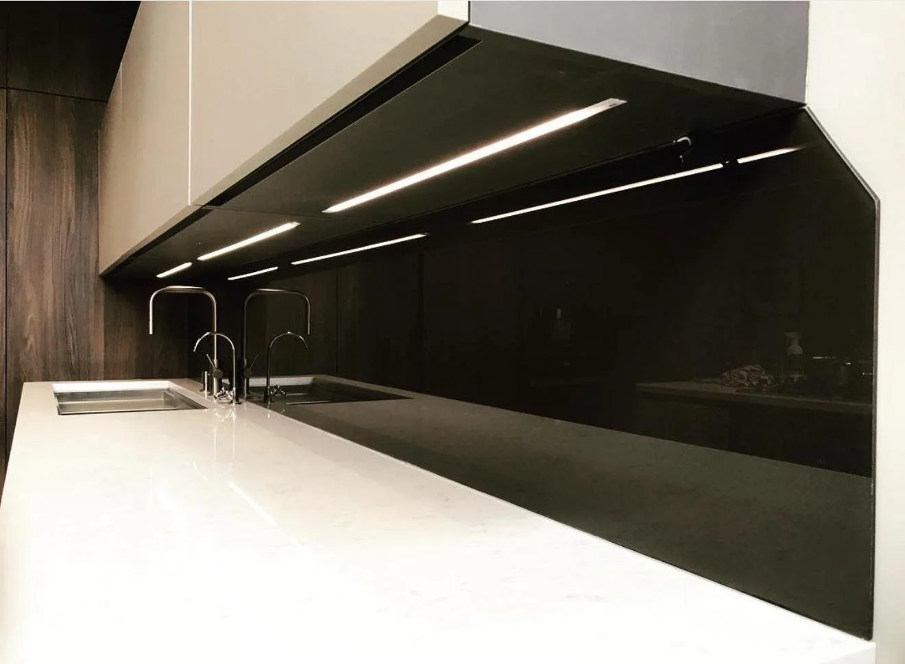Modern kitchen countertop with sink and chrome faucet, black backsplash, upper cabinets, and under-cabinet lighting.