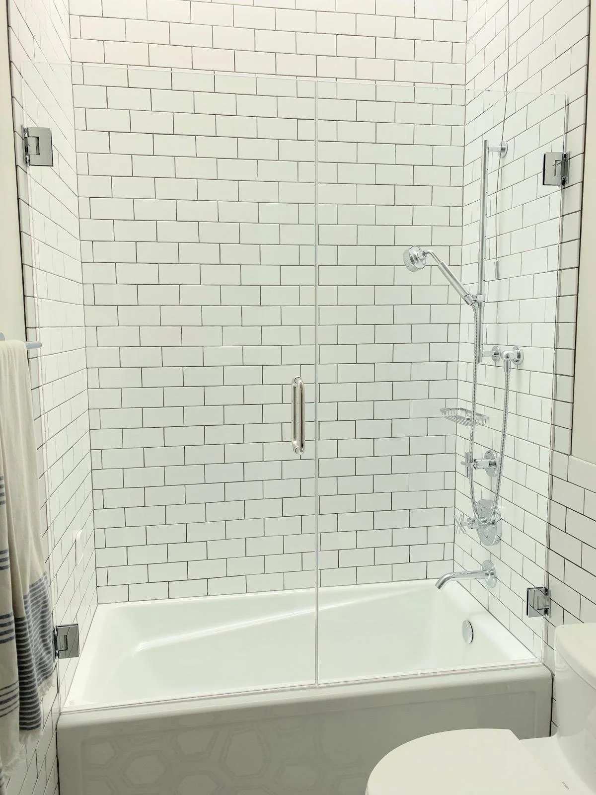 A bathroom with a glass shower enclosure, white subway tile walls, and a toilet in the foreground.