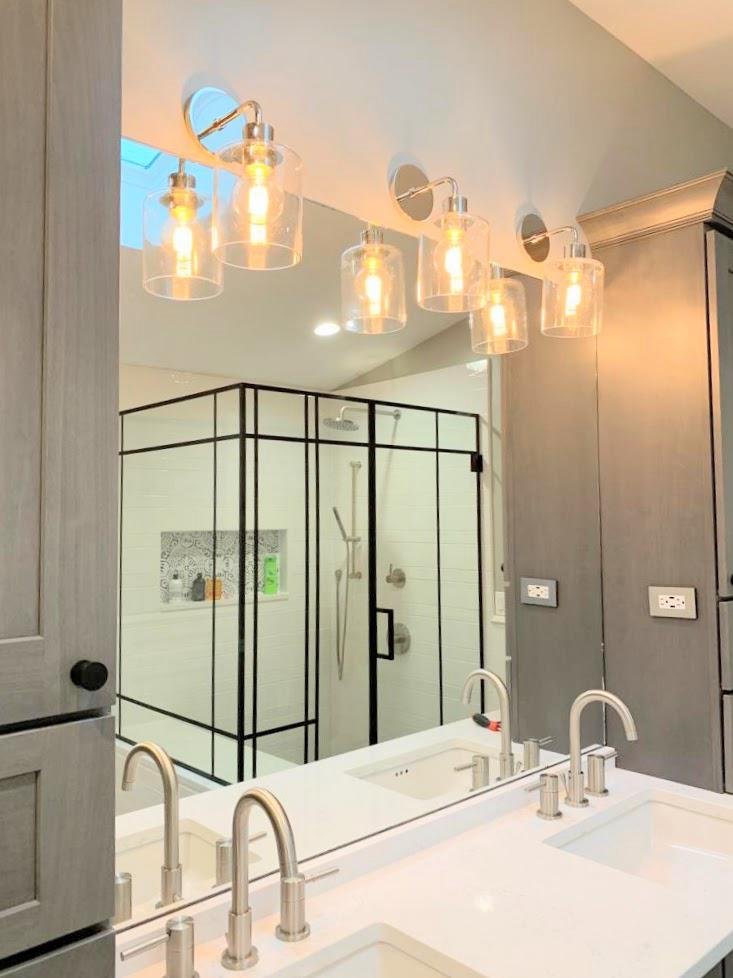 Modern bathroom with a double sink vanity, four glass-bracketed light fixtures, and a glass-enclosed shower with black trim.