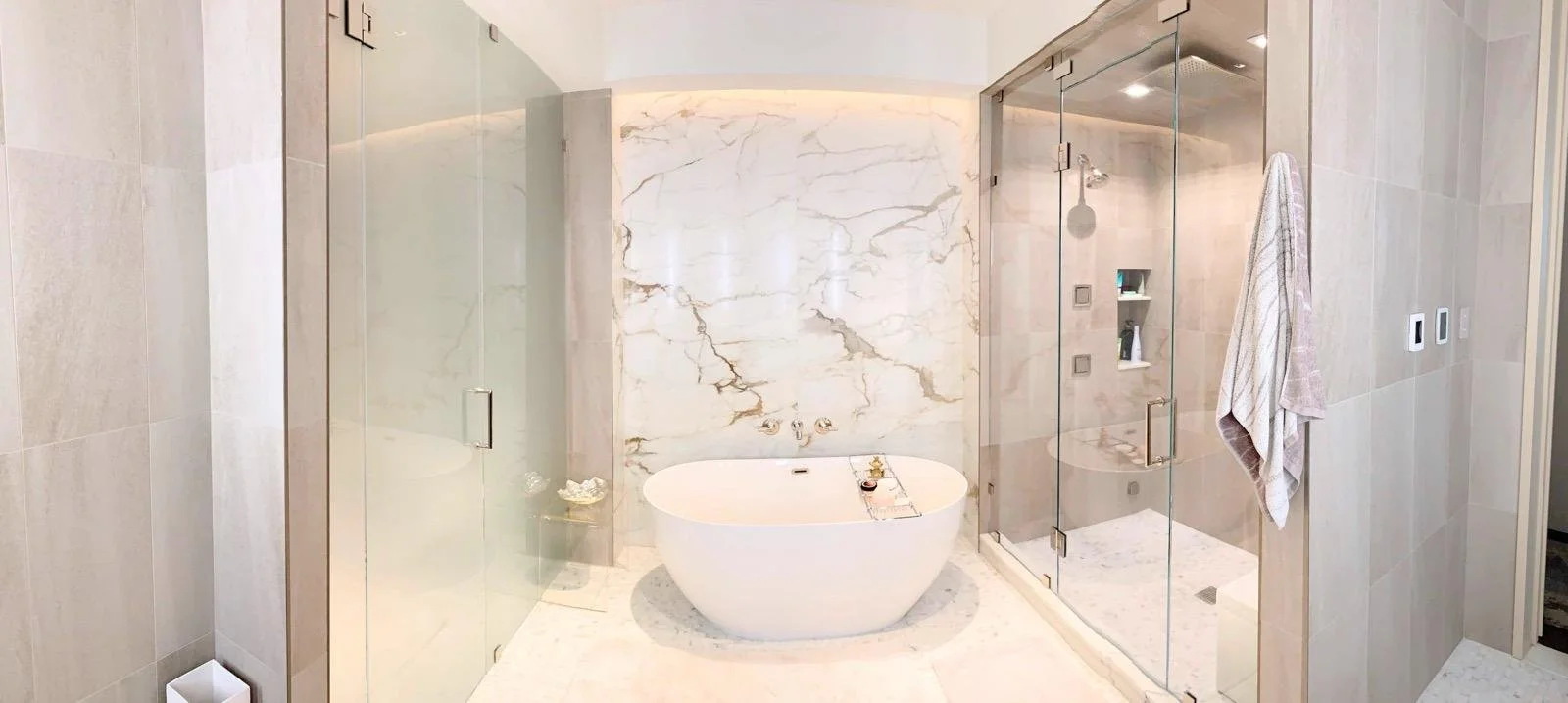 Modern bathroom with a freestanding bathtub, large marble wall, and separate glass-enclosed shower with beige tiles and a towel hanging on the wall.