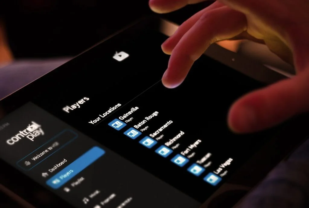 Close-up of a person selecting a location on a gaming app called 'Control Play' on a tablet, with a list of cities including Gainesville, Baton Rouge, Sacramento, Richmond, and Fort Myers.