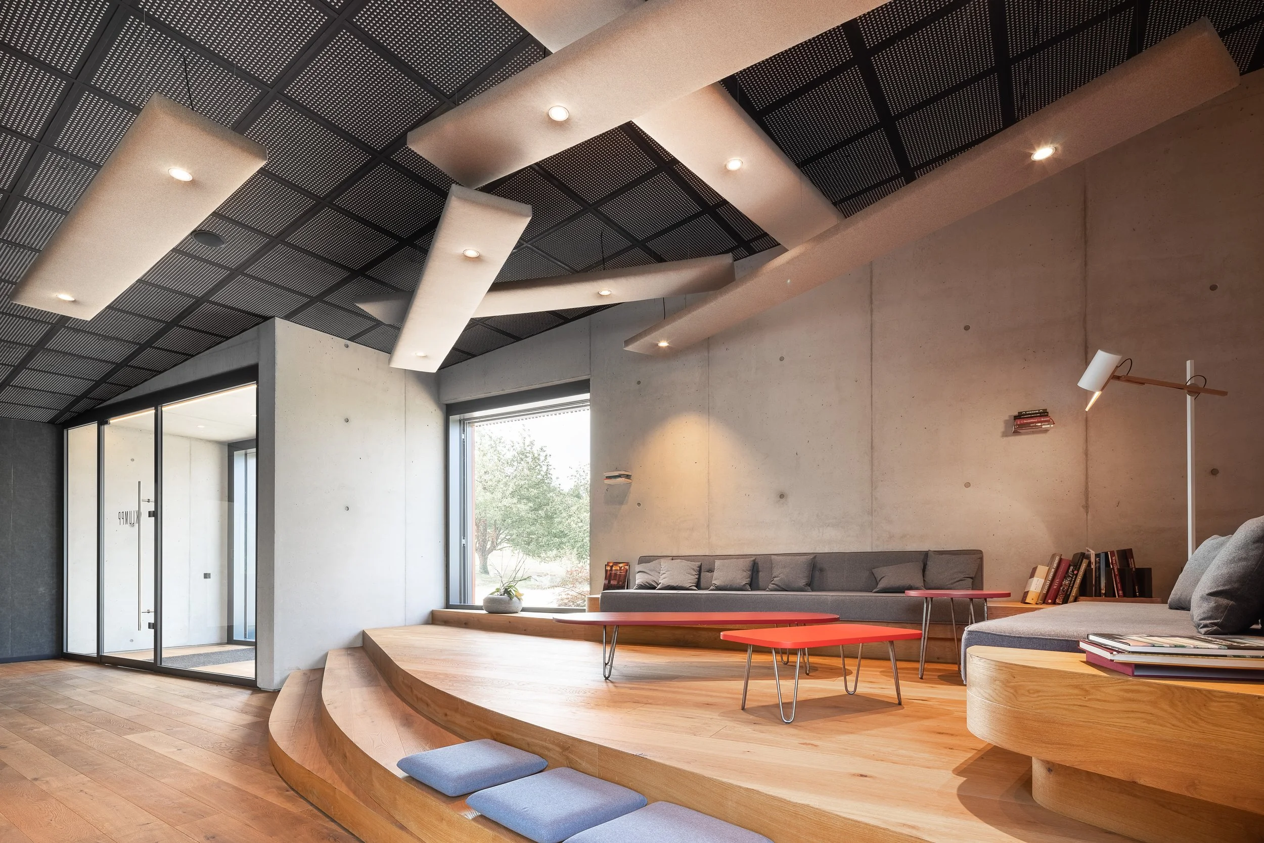 Moderner Wohnzimmerbereich mit Hochsitz, Sofa, Büchern und großem Fenster, hoher Decke mit integrierten Lichtern und Kiefernholz-Boden