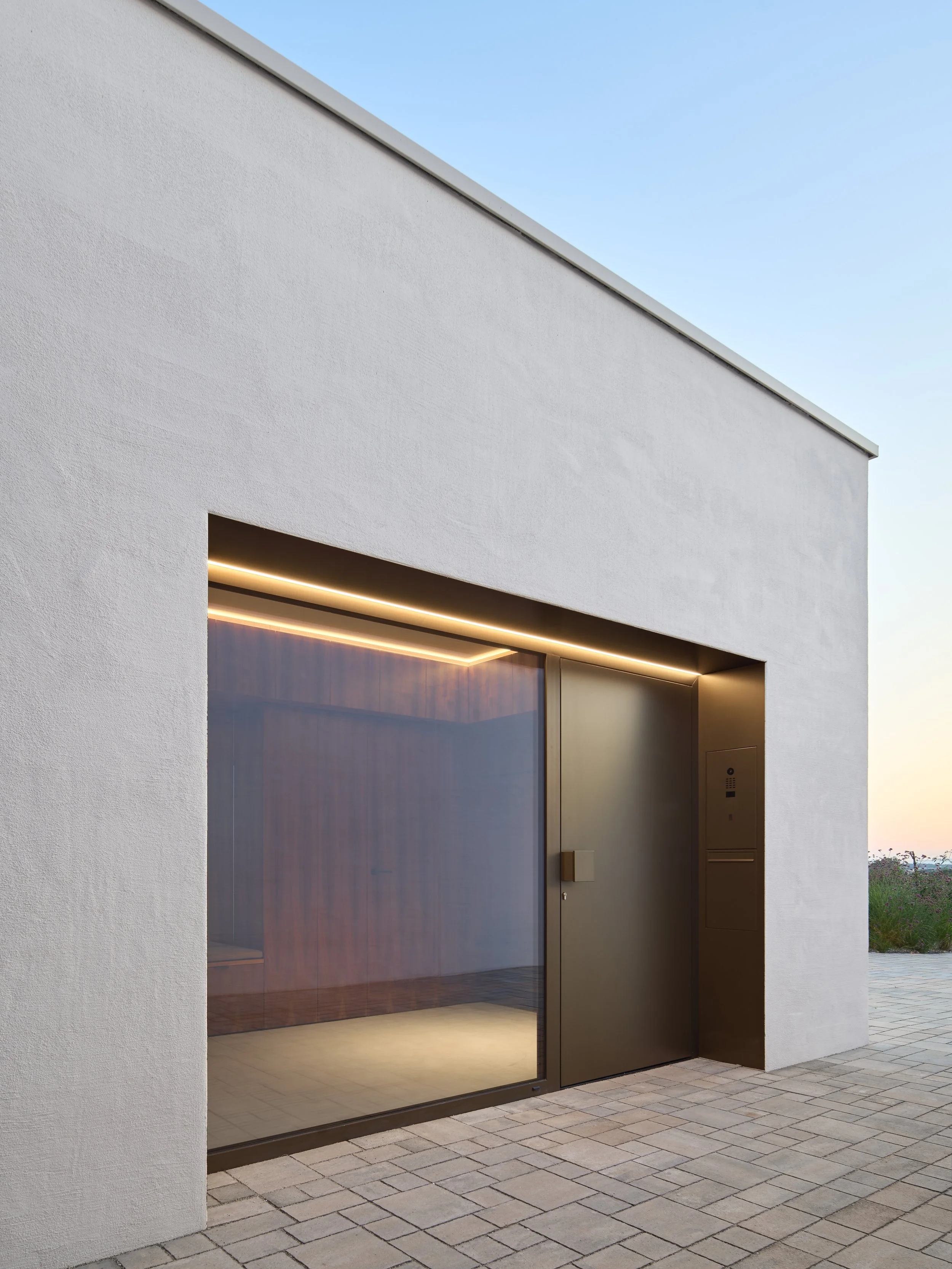 Modernes Gebäude mit großen Glasfenstern und minimalistischem Design, Außenanlage mit Pflastersteinen, bei Sonnenuntergang