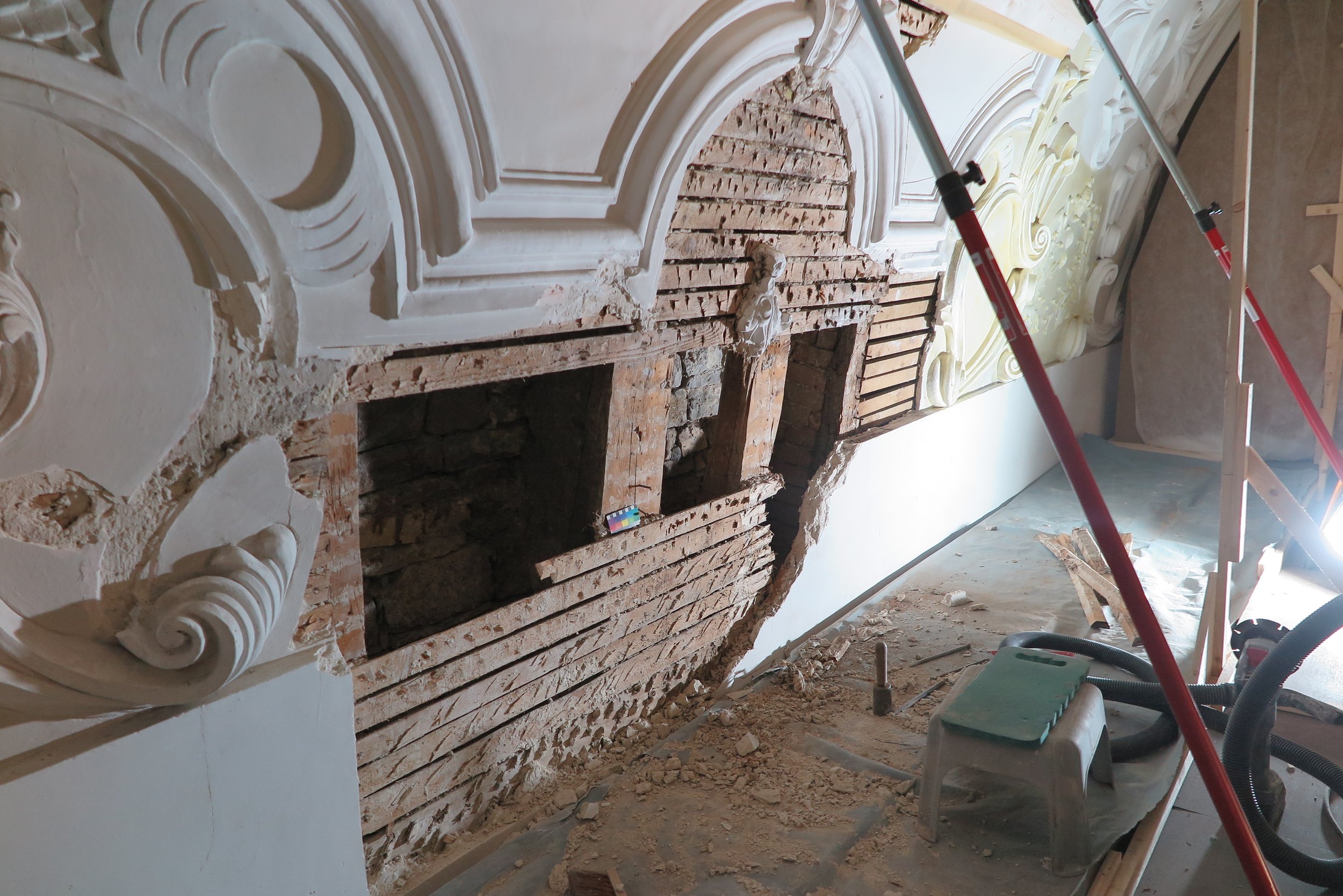 Innenaufnahme eines Renovierungsprojekts an einer Wand mit aufbereiteter, verzierte Wandarchitektur, die teilweise abgetragen ist, inklusive Bauwerkzeuge und Baumaterialien.