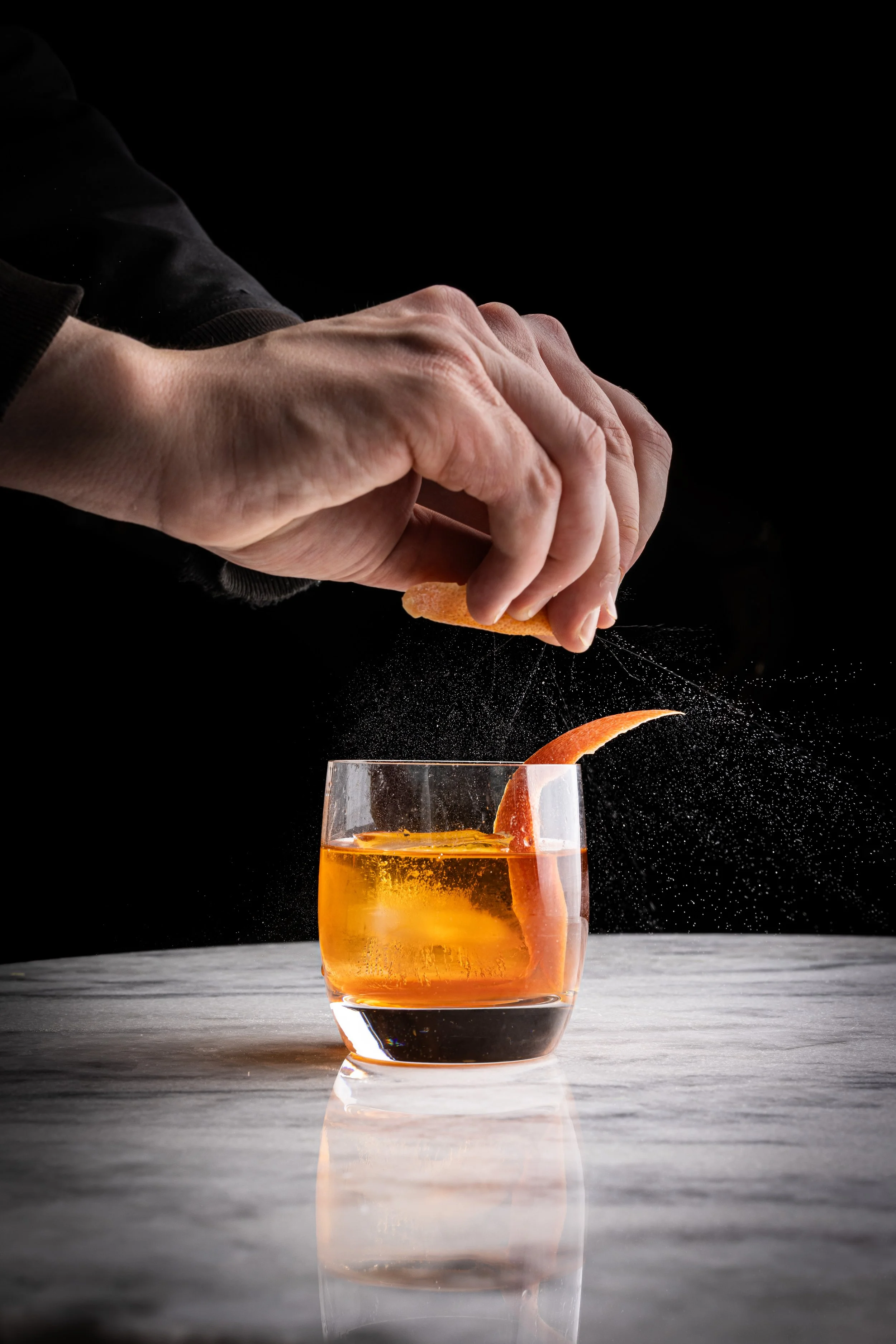 A bartender spritzing citrus zest on a cocktail