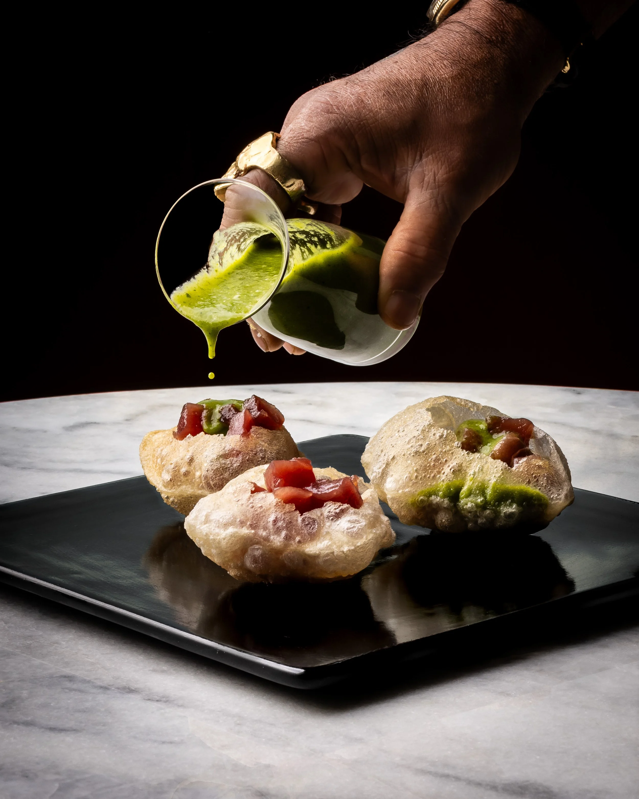 A chef pouring a green sauce over a plate of food