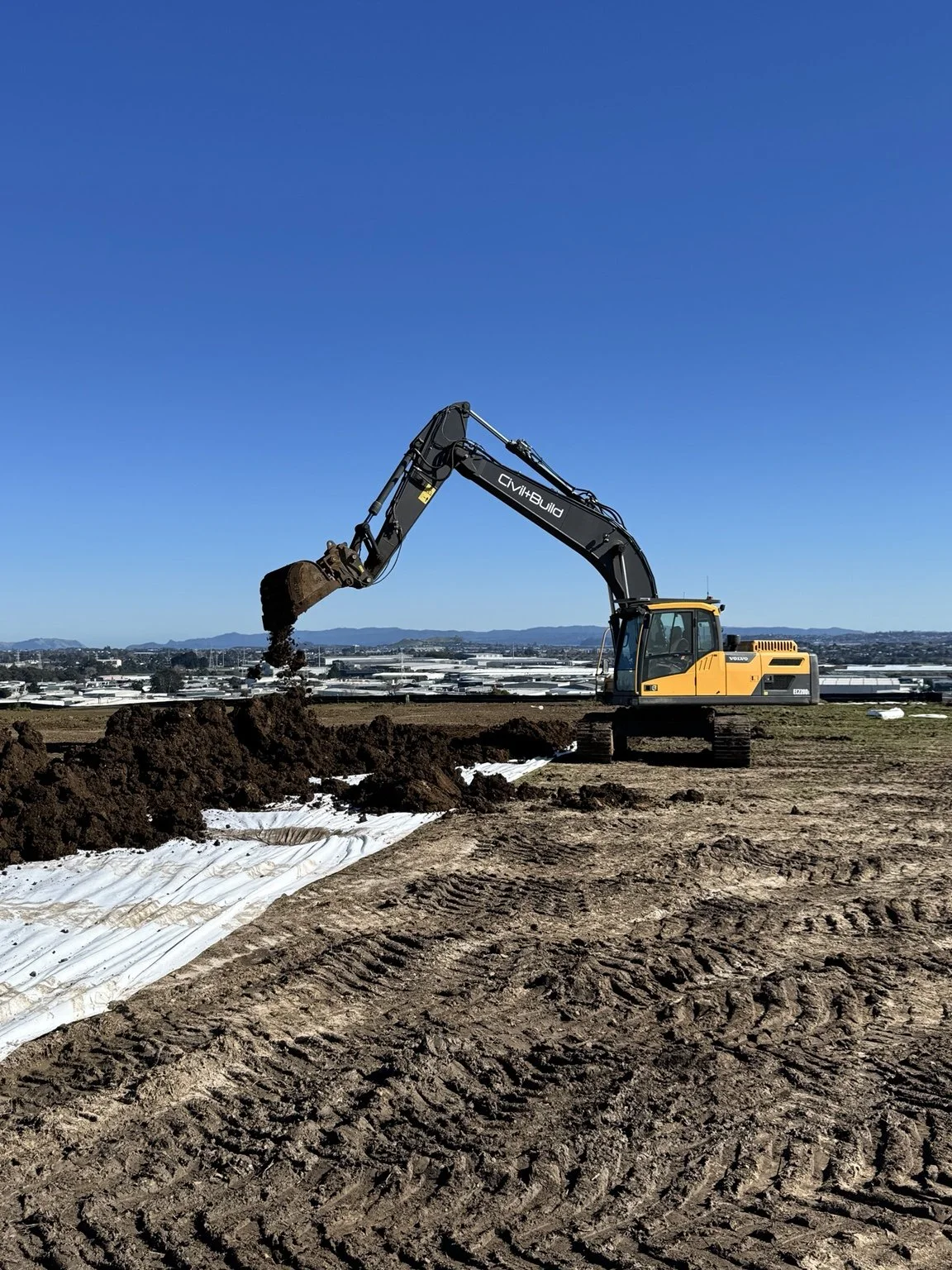 Yellow Volvo excavator digging soil at a construction site under a clear blue sky