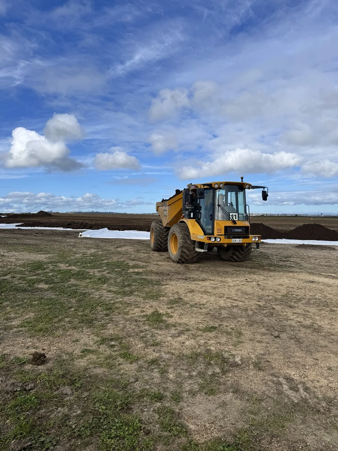 Yellow articulated dump truck at a construction site beneath a blue, cloud-filled sky