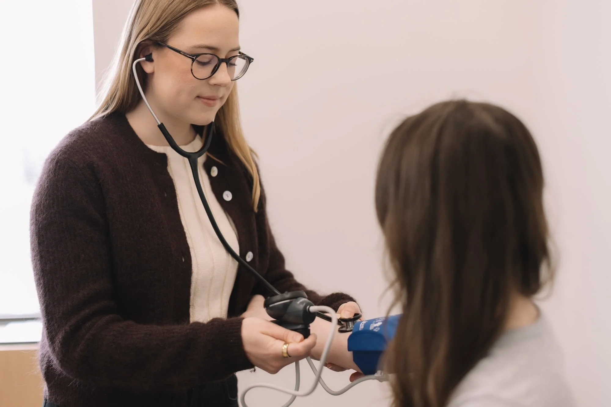 A female healthcare provider with glasses using a stethoscope to check a child's heartbeat in a clinic or medical setting.