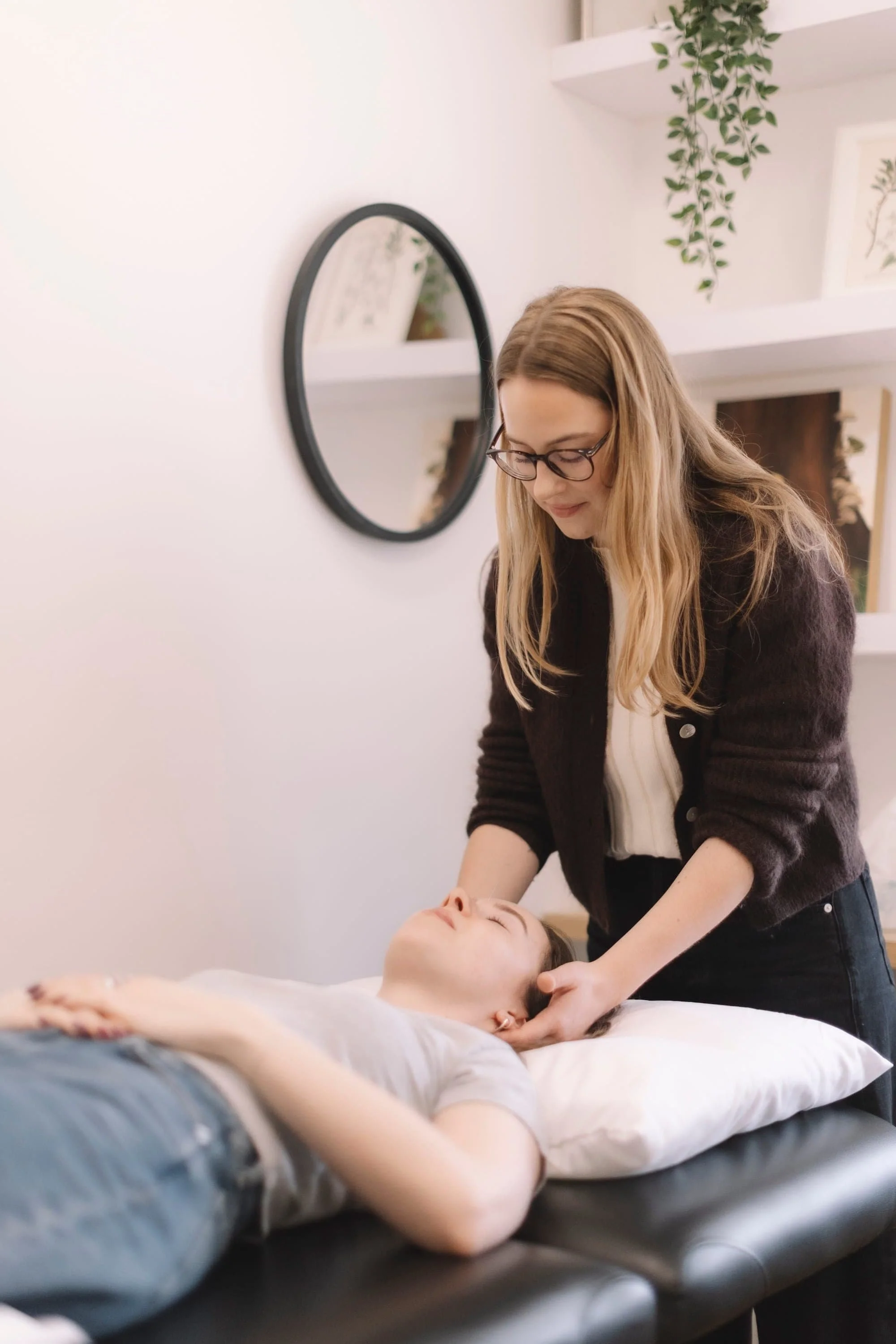 A woman providing a massage or reiki treatment to a person lying on a massage table in a calming, decorated room.