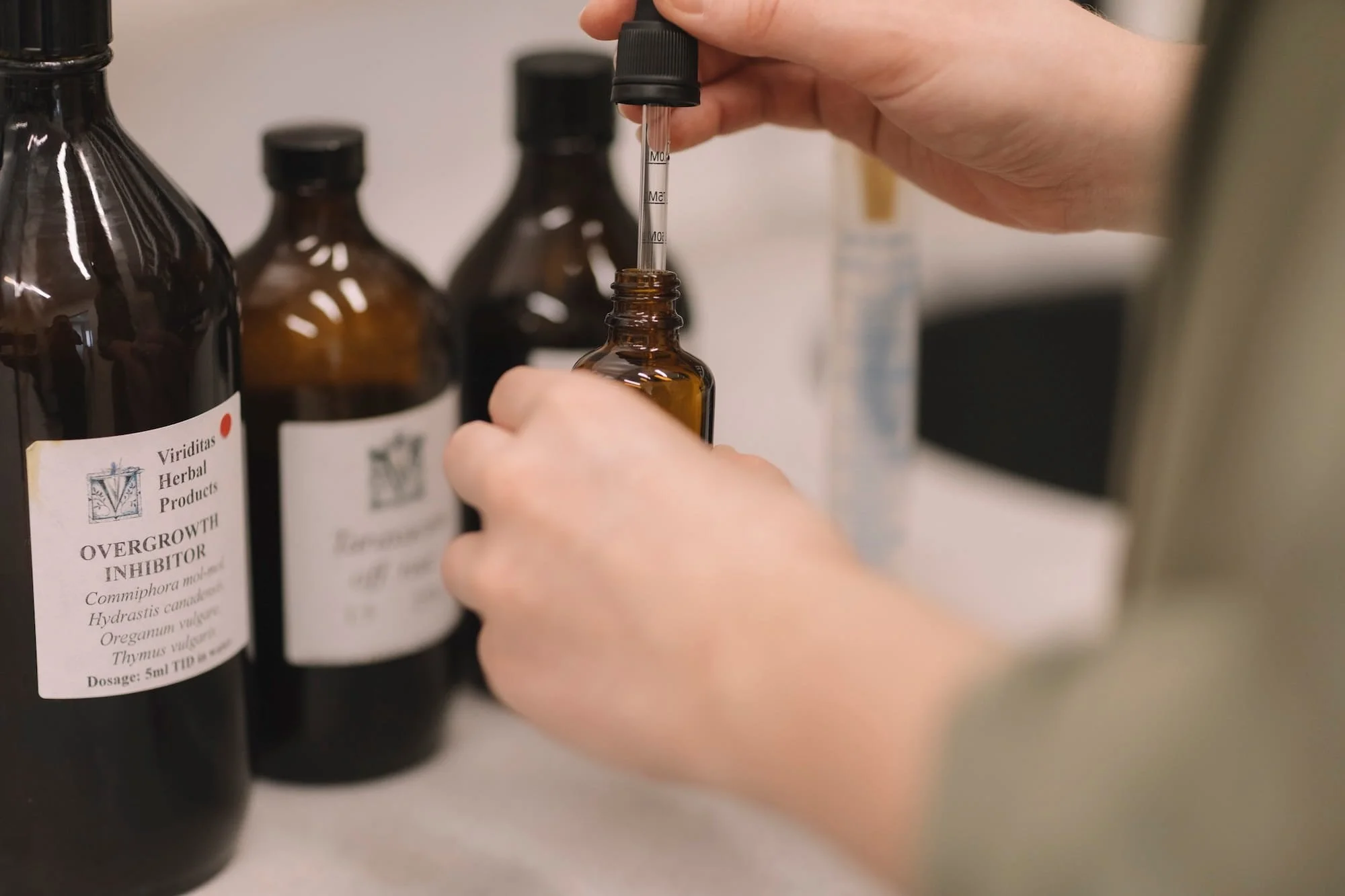 Close-up of a person using a dropper to transfer liquid into an amber glass bottle, with additional amber bottles in the background.