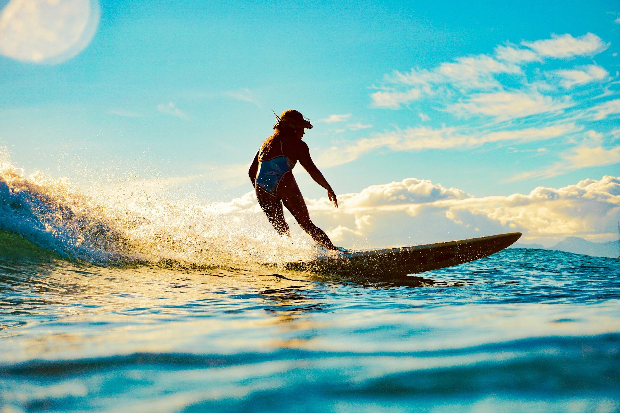 A person surfing on a wave in the ocean during a sunny day with a partly cloudy sky.