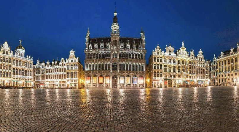 Square in front of ornate, historic buildings with a central tower against a dark blue evening sky.