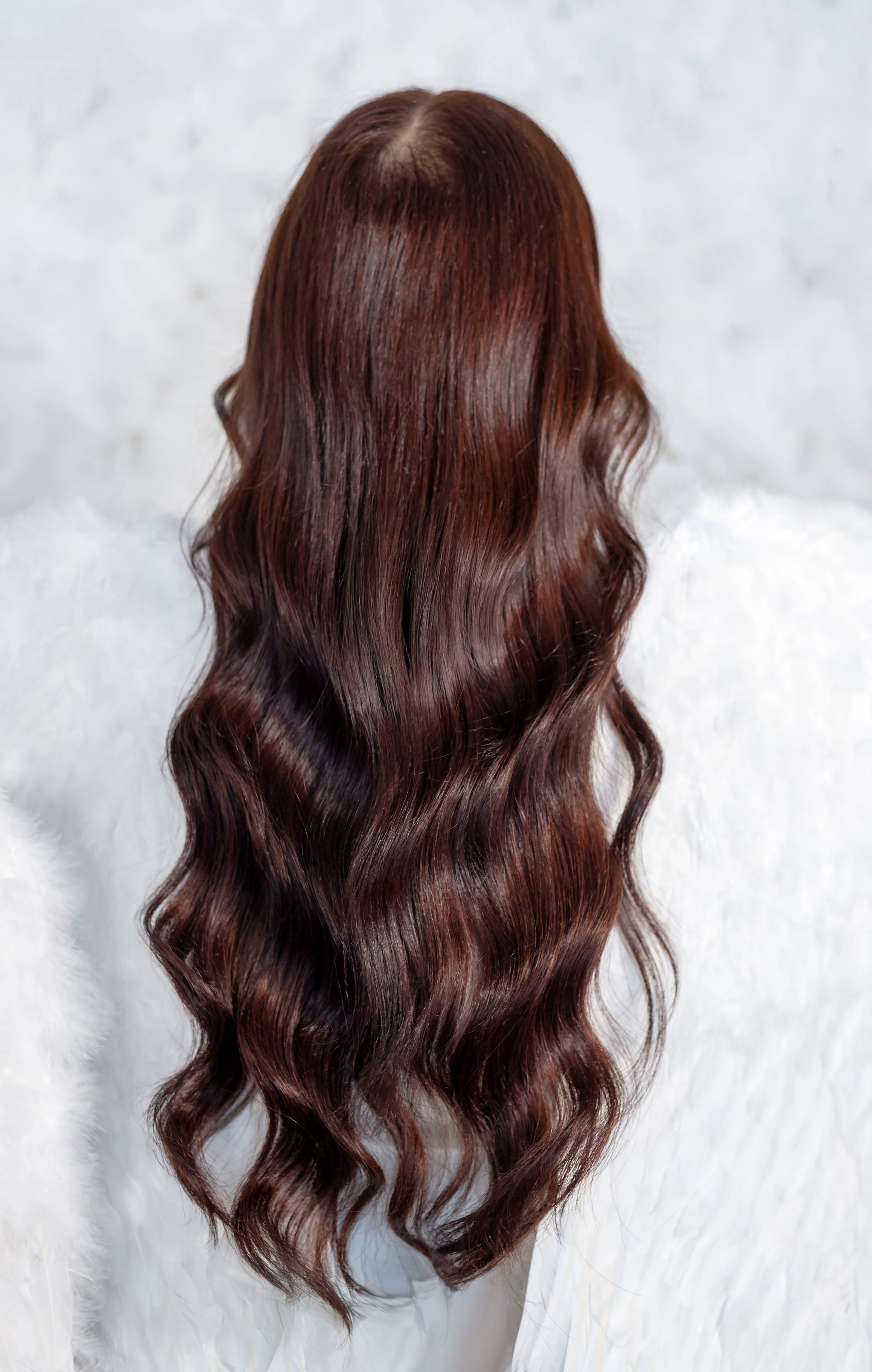 Long, wavy, reddish-brown hair on a person with their back to the camera, against a white background.
