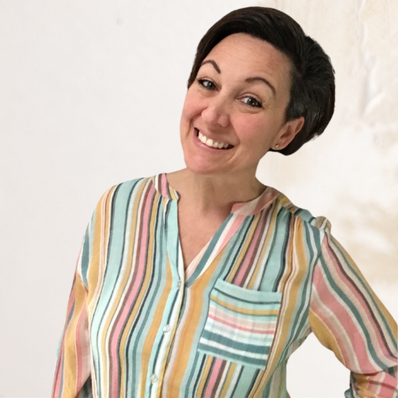 A woman with short dark hair smiling, wearing a colorful vertical striped shirt with pastel shades, in front of a plain white background.