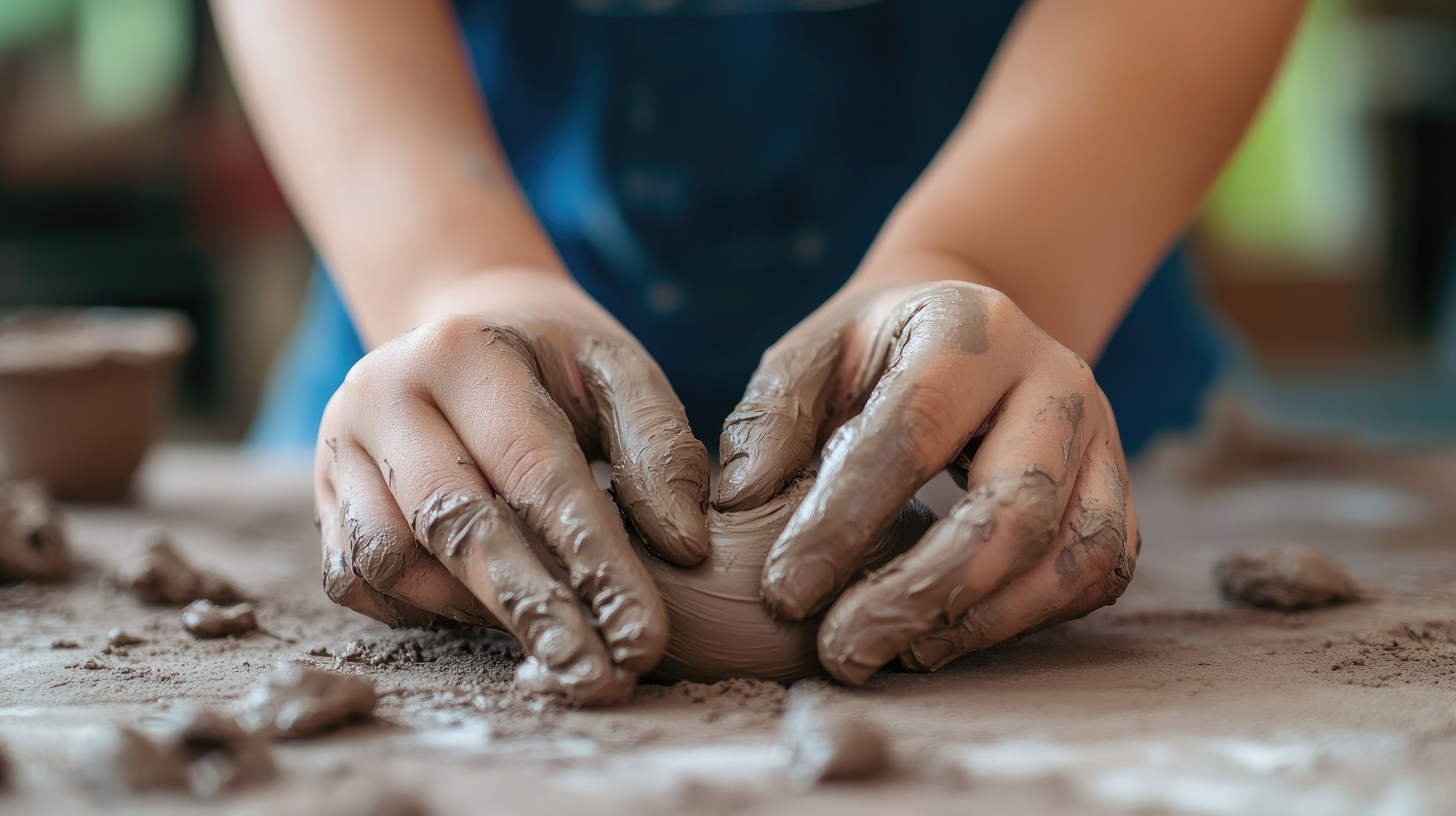 Person shaping clay with hands, working on a pottery piece at a workstation.
