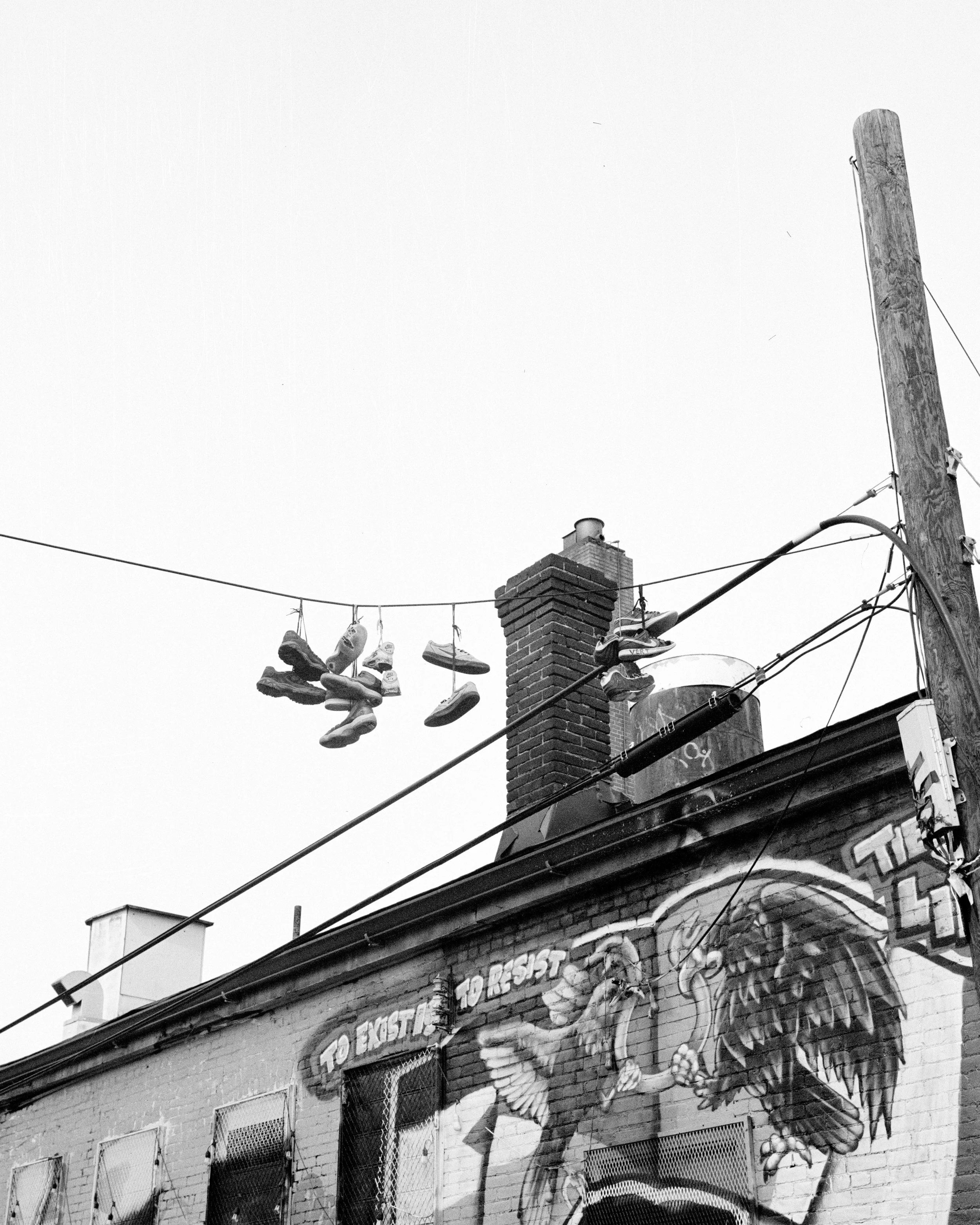 A black and white photo of a building with a mural featuring an eagle and a bird, and shoes hanging on a wire above.
