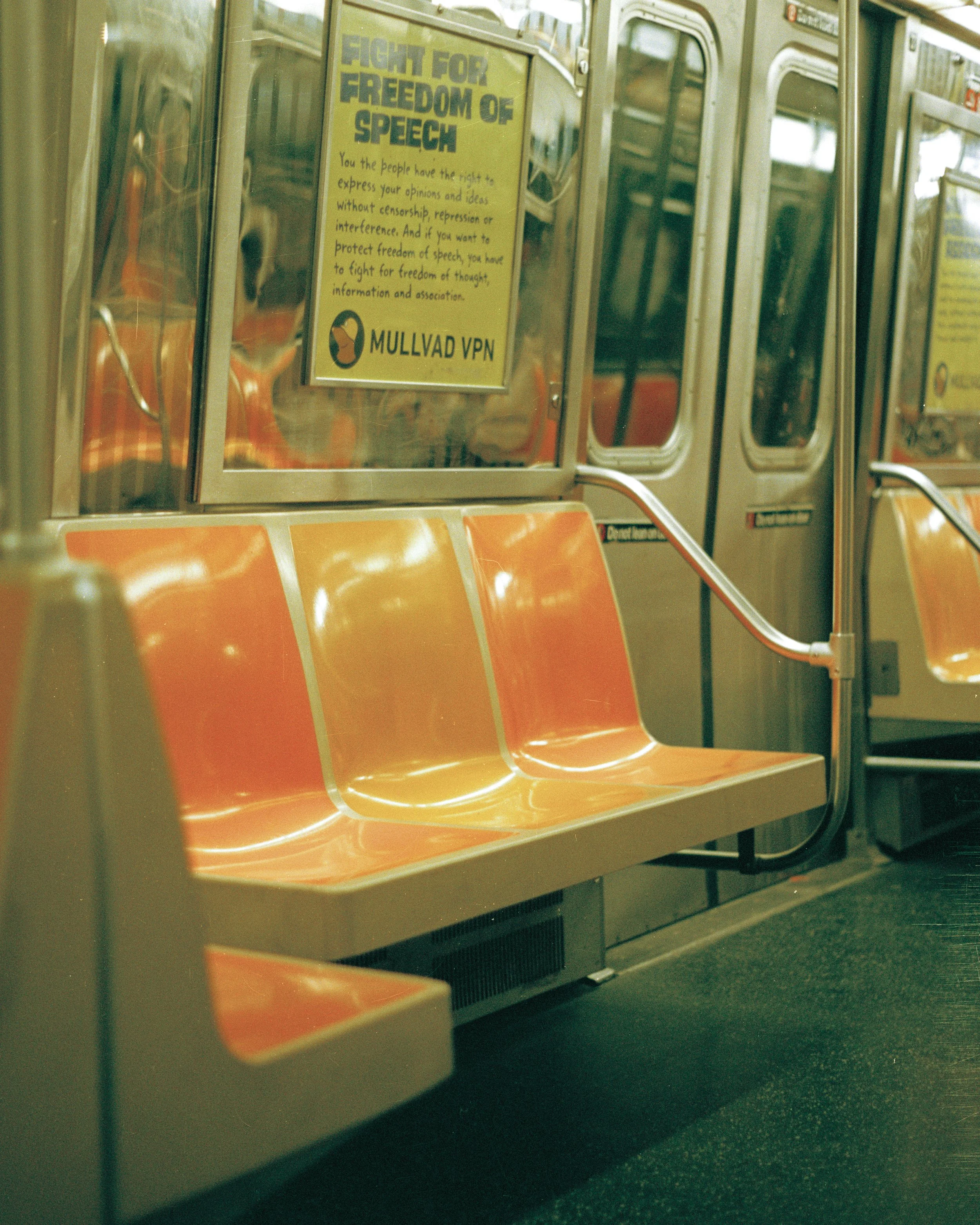 Empty orange subway seats, a yellow sign about freedom of speech, and closed subway doors.