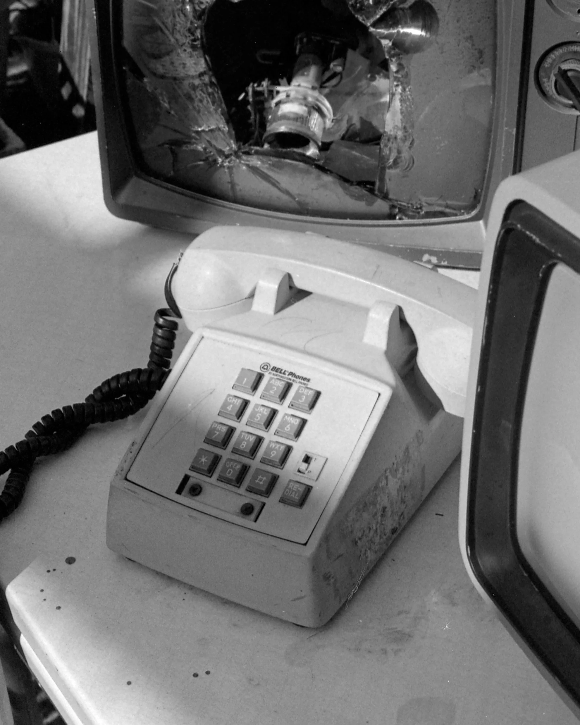 Old rotary desk phone with a broken cracked screen on the receiver, with a dusty surface, next to an old microwave oven.