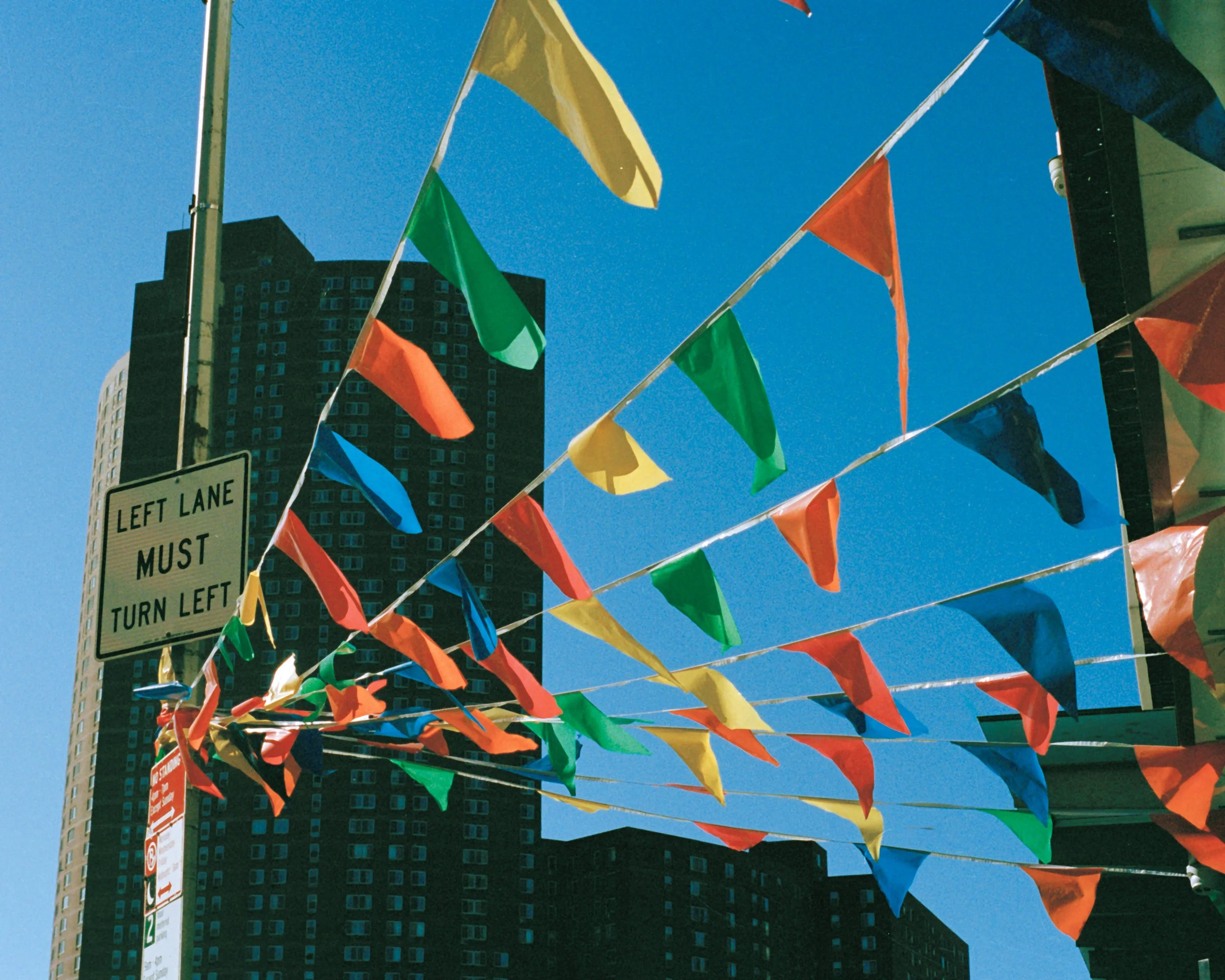 Colorful pennant flags hanging across the street with a tall building and a clear blue sky in the background.