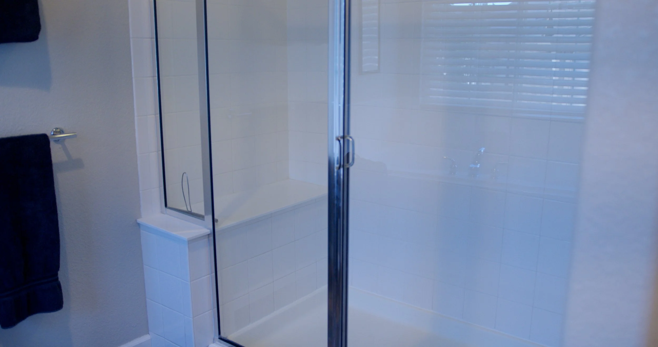 Bathroom shower with glass doors, white tiled walls, and a window with blinds