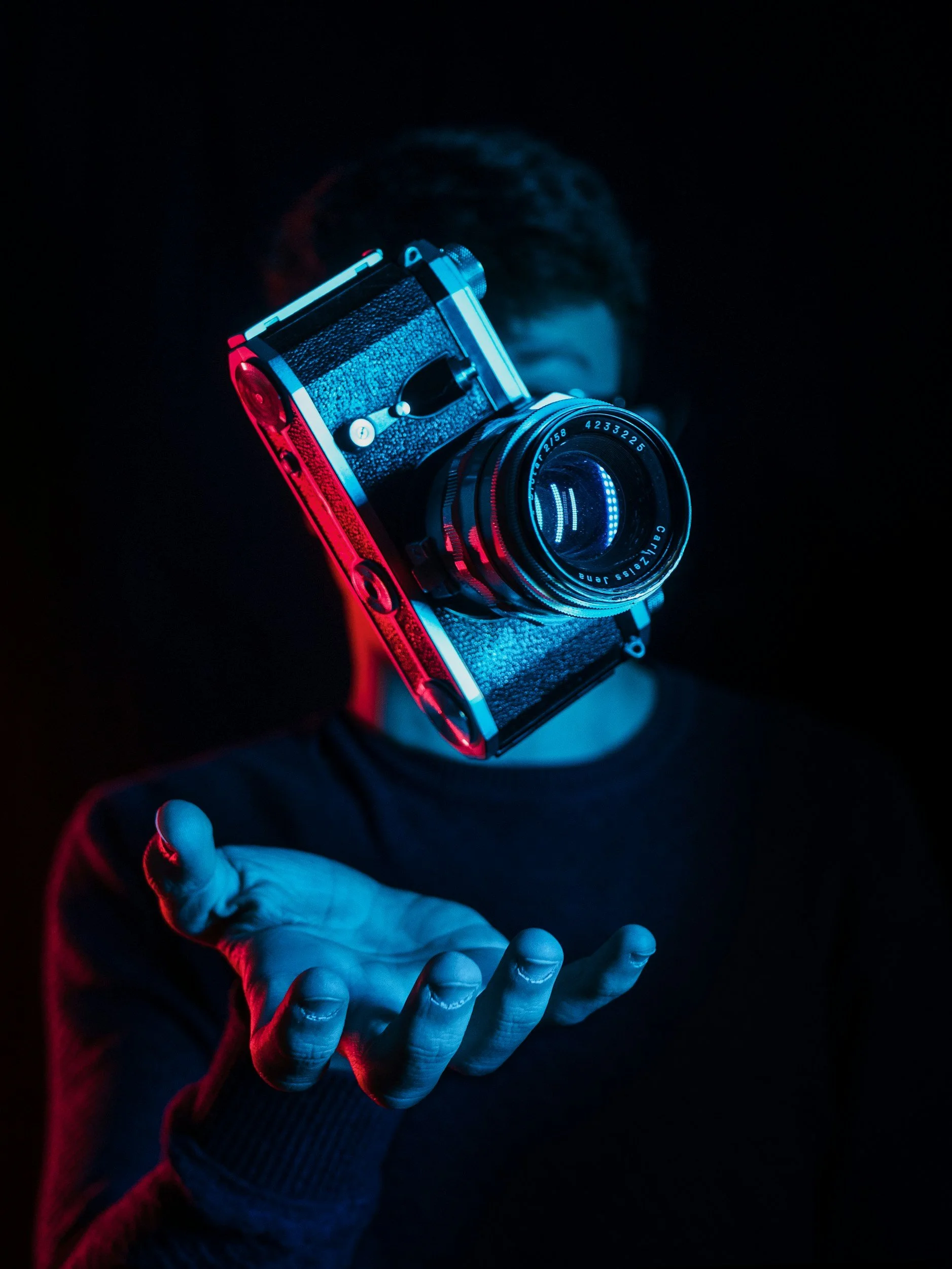 Person with a camera in front of their face, illuminated with blue and red lighting, in a dark setting.