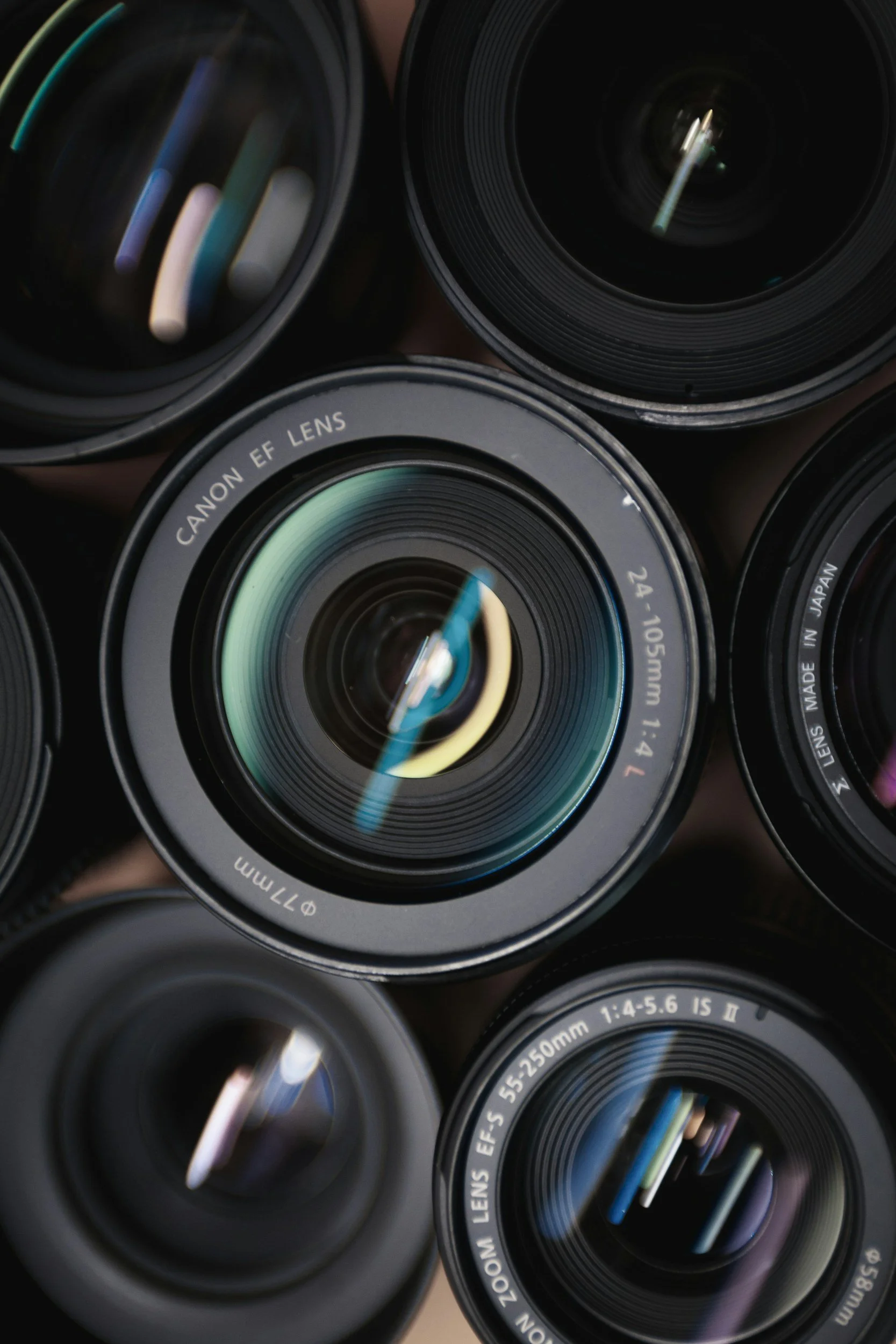 Close-up of multiple camera lenses, including a Canon EF lens with focal length 24-105mm and an EF-S lens with focal length 55-250mm.