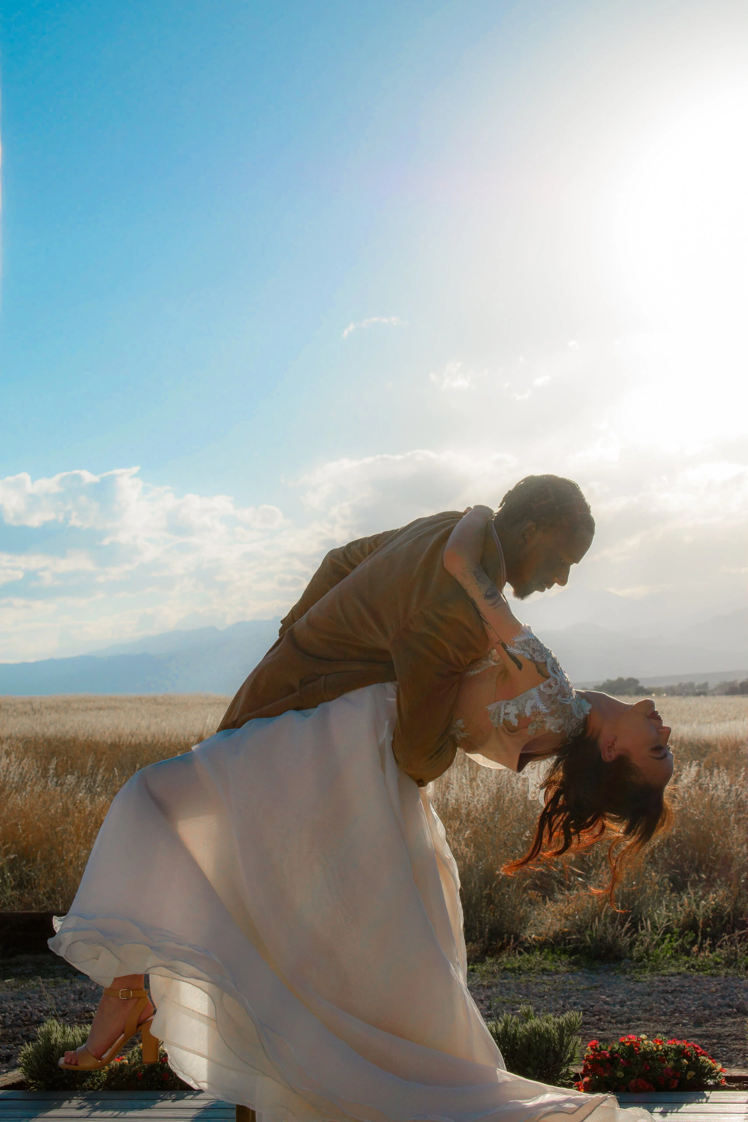 A couple dancing outdoors during sunset in a field, with the man dipping the woman and both smiling.