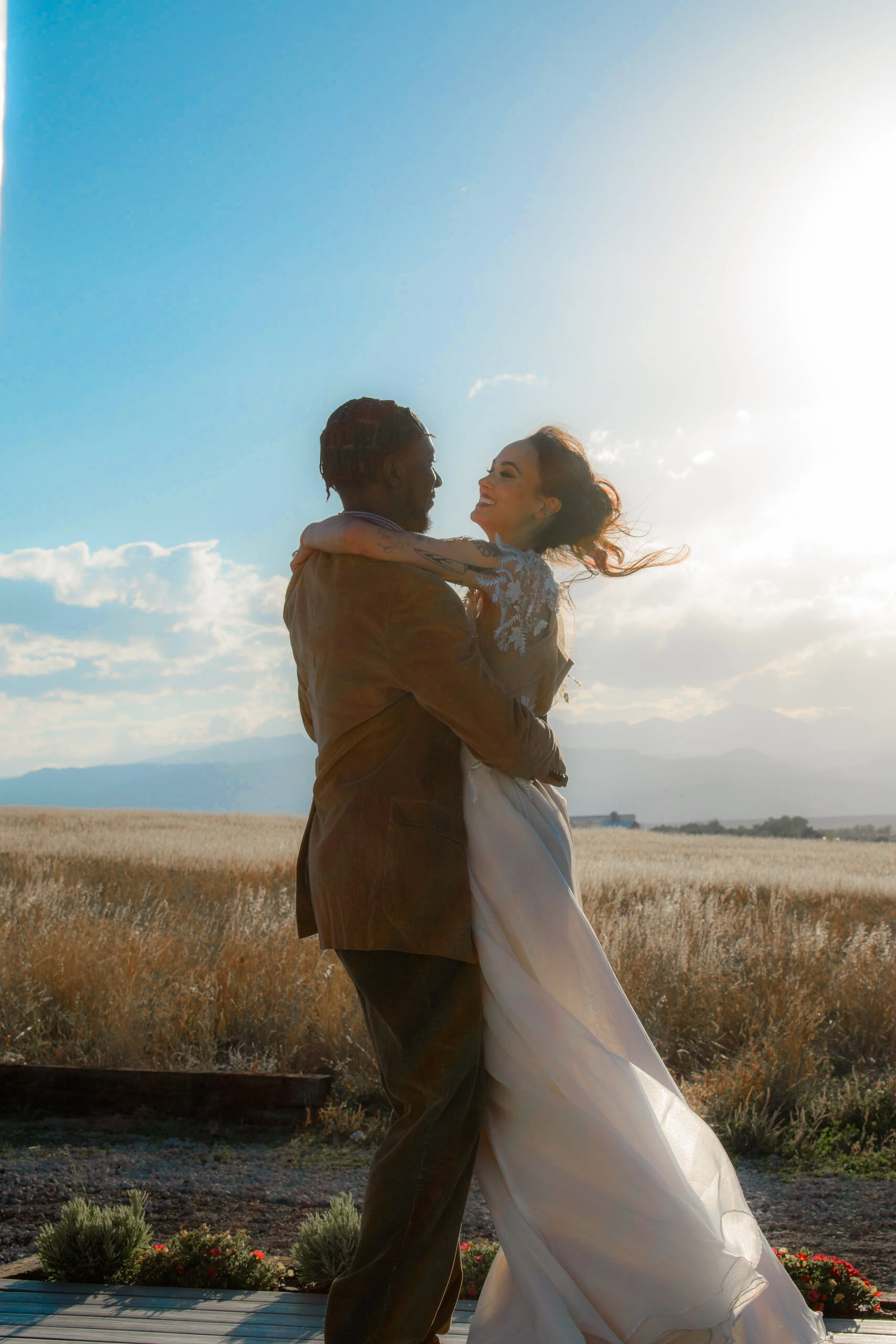 A couple in wedding attire dancing outdoors during sunset in a rural field.