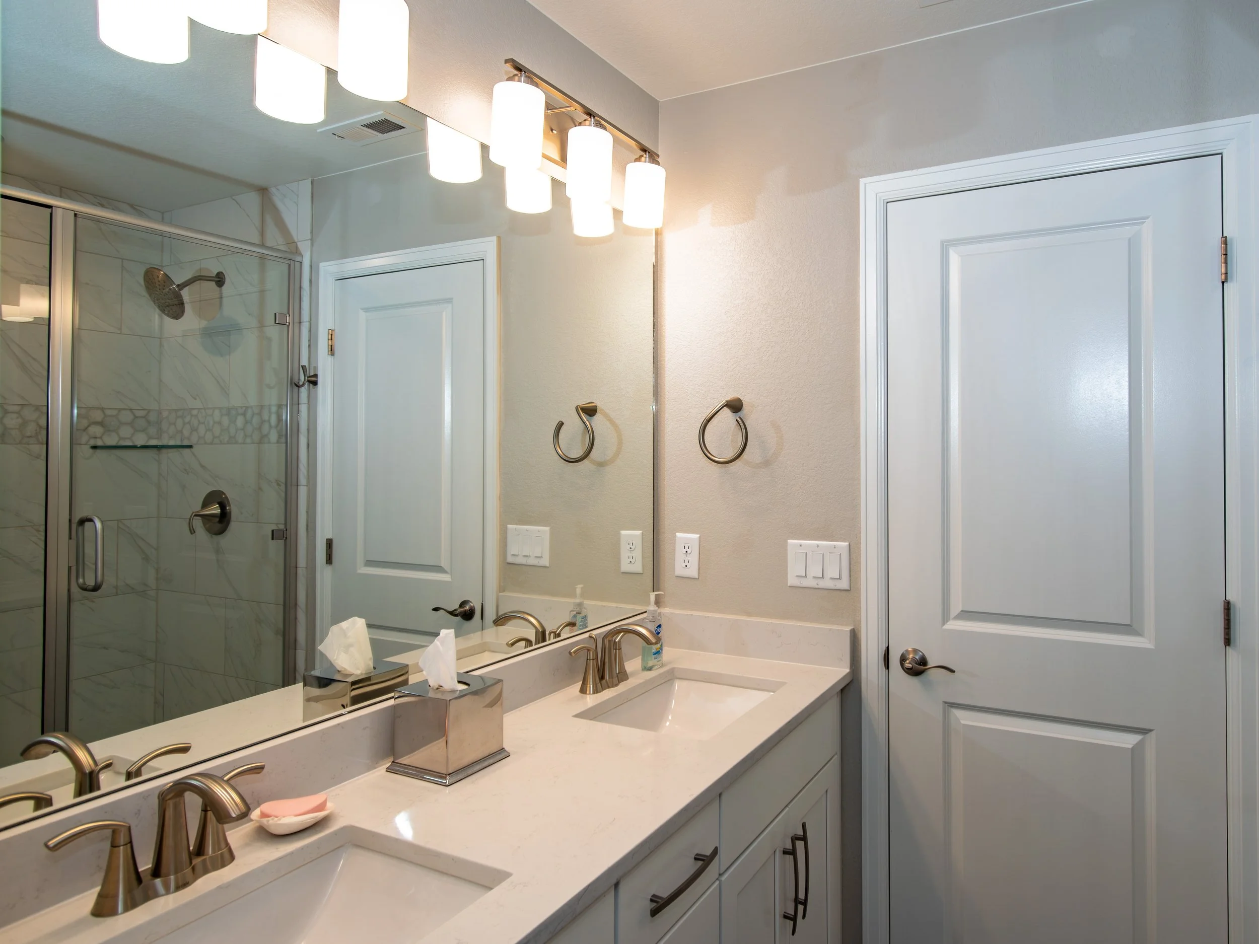Bathroom with double sinks, a large mirror, and a tiled shower with a glass enclosure.