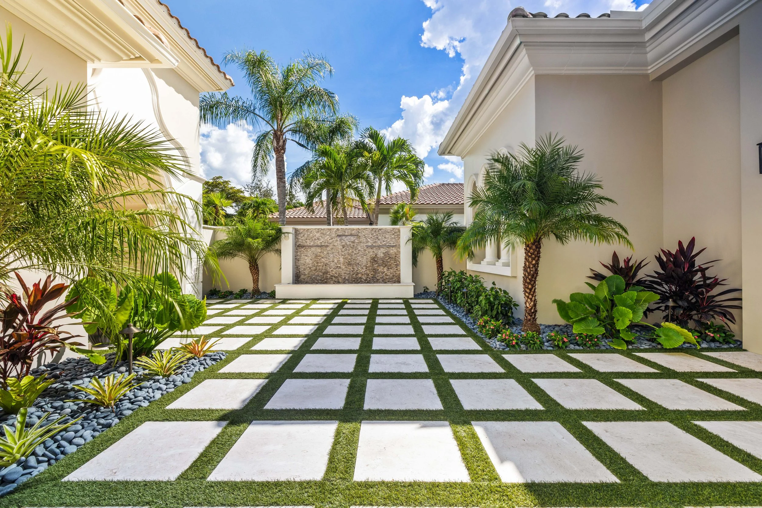 Square turf paver courtyard framed by hedges and modern palms with water feature focal point.
