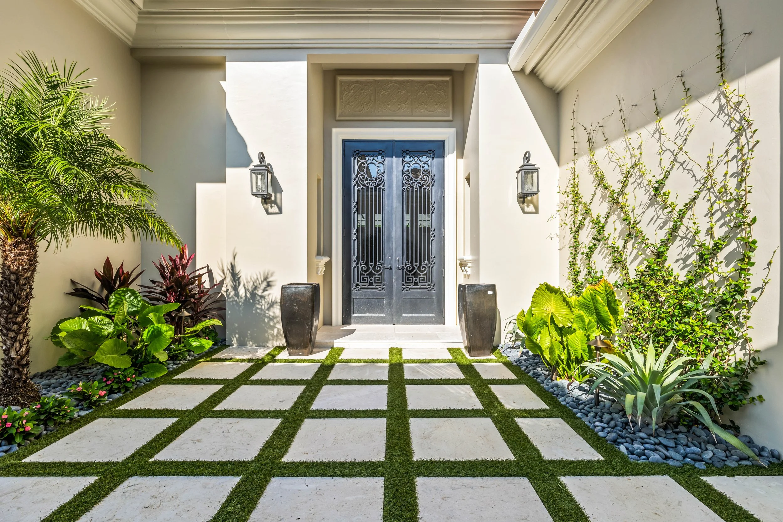 Symmetrical entry view with grid-style turf pavers leading to glass and wrought-iron front door.