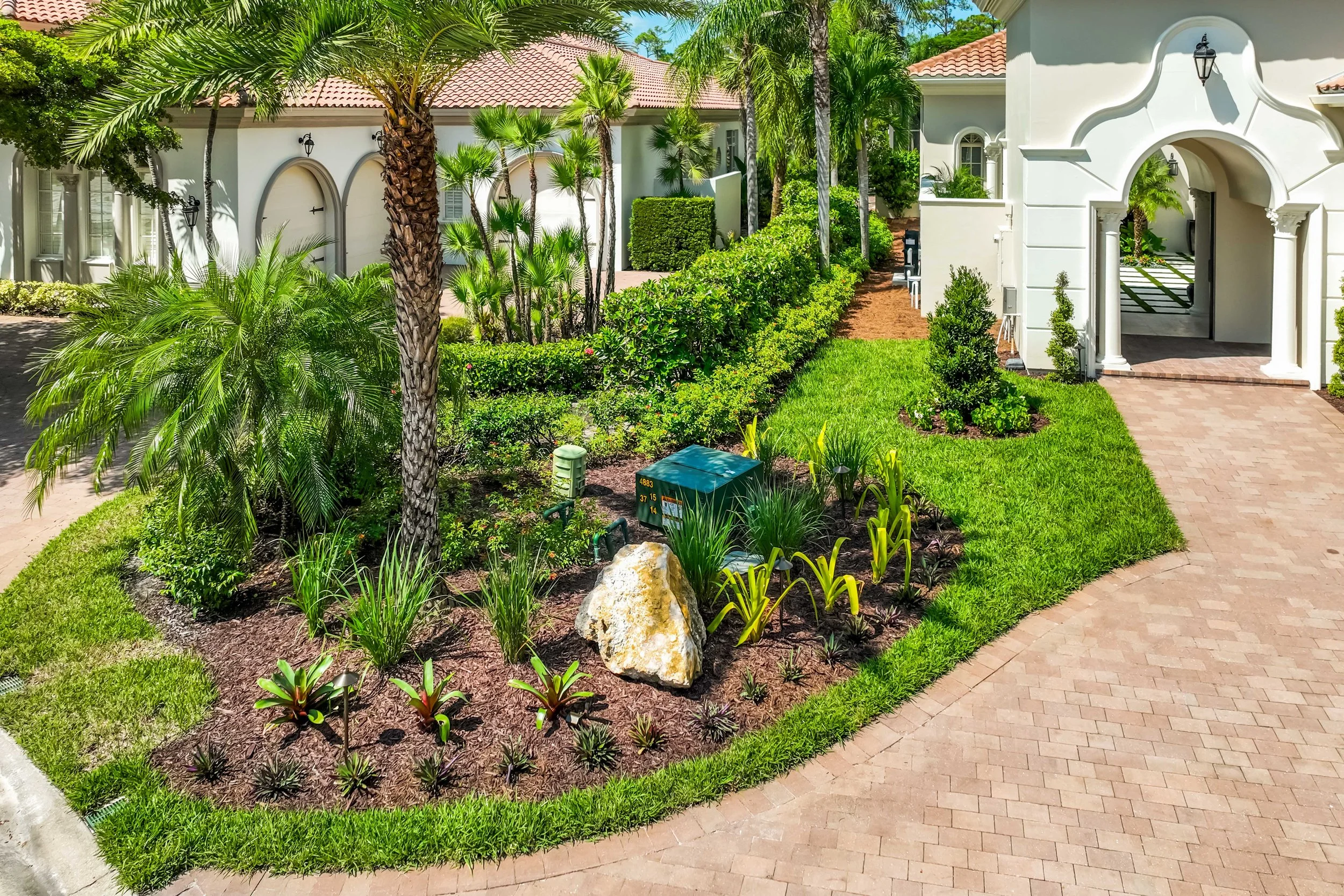Tropical landscape island with decorative boulders, palm trees, and colorful underplantings.