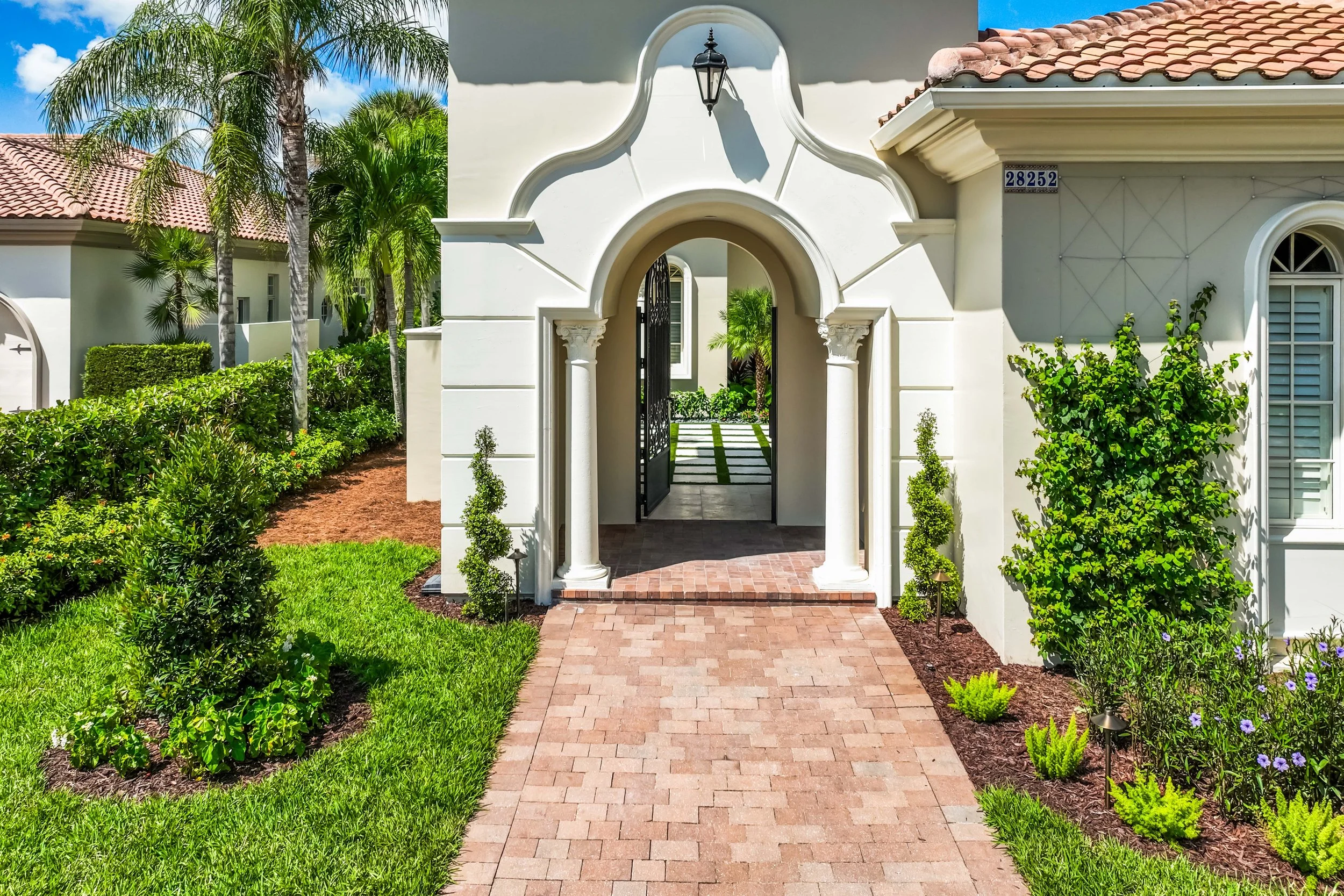 Estate-style arched entry with symmetrical landscape lighting and vertical planting flanking the door.