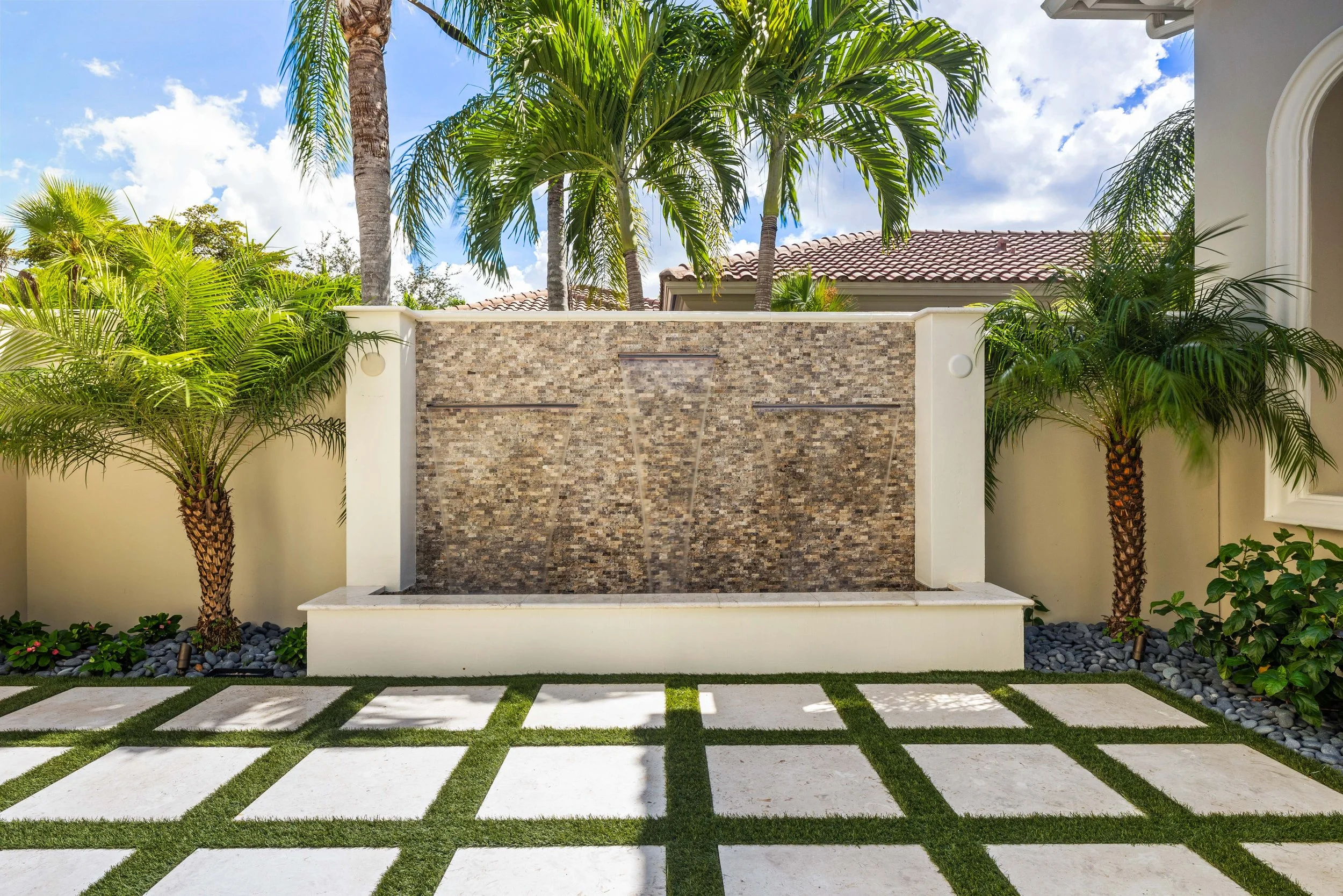 Outdoor water feature wall with stacked stone finish and tropical plant backdrop.