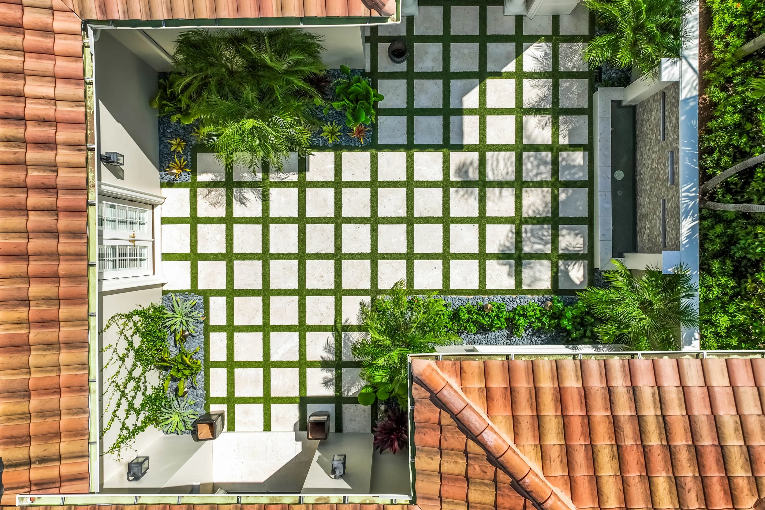 Overhead view of geometric turf and concrete grid patio surrounded by lush planters.