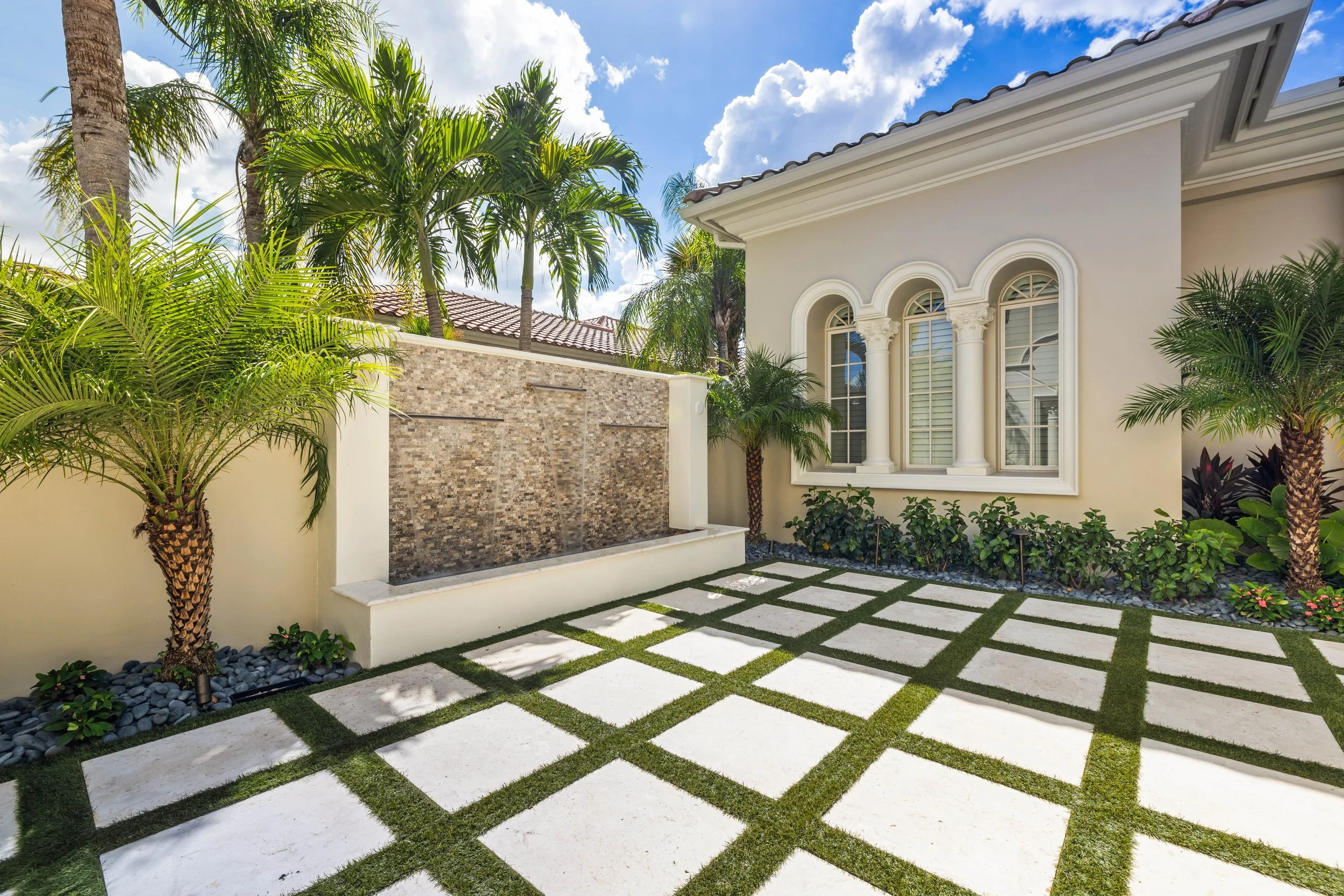 Tile-accented water wall and modern grid paver courtyard at luxury Florida home.